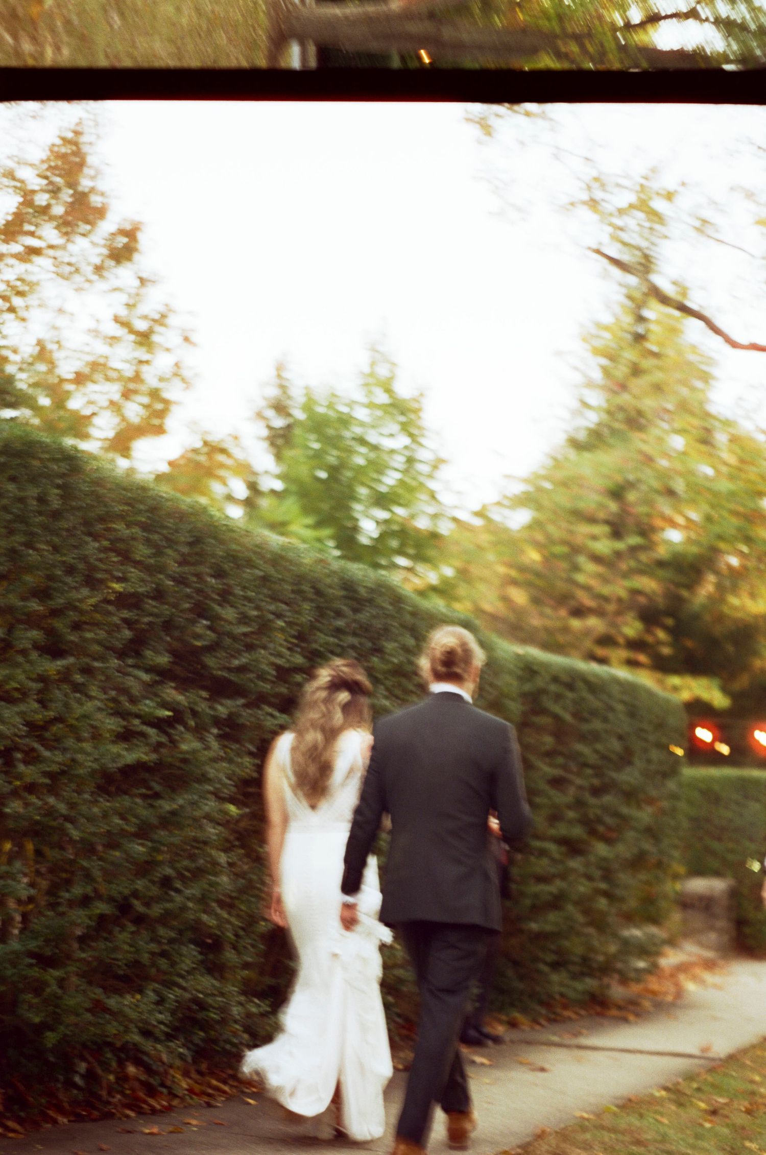 A couple walking away on a garden path, with the bride in white and groom in black.