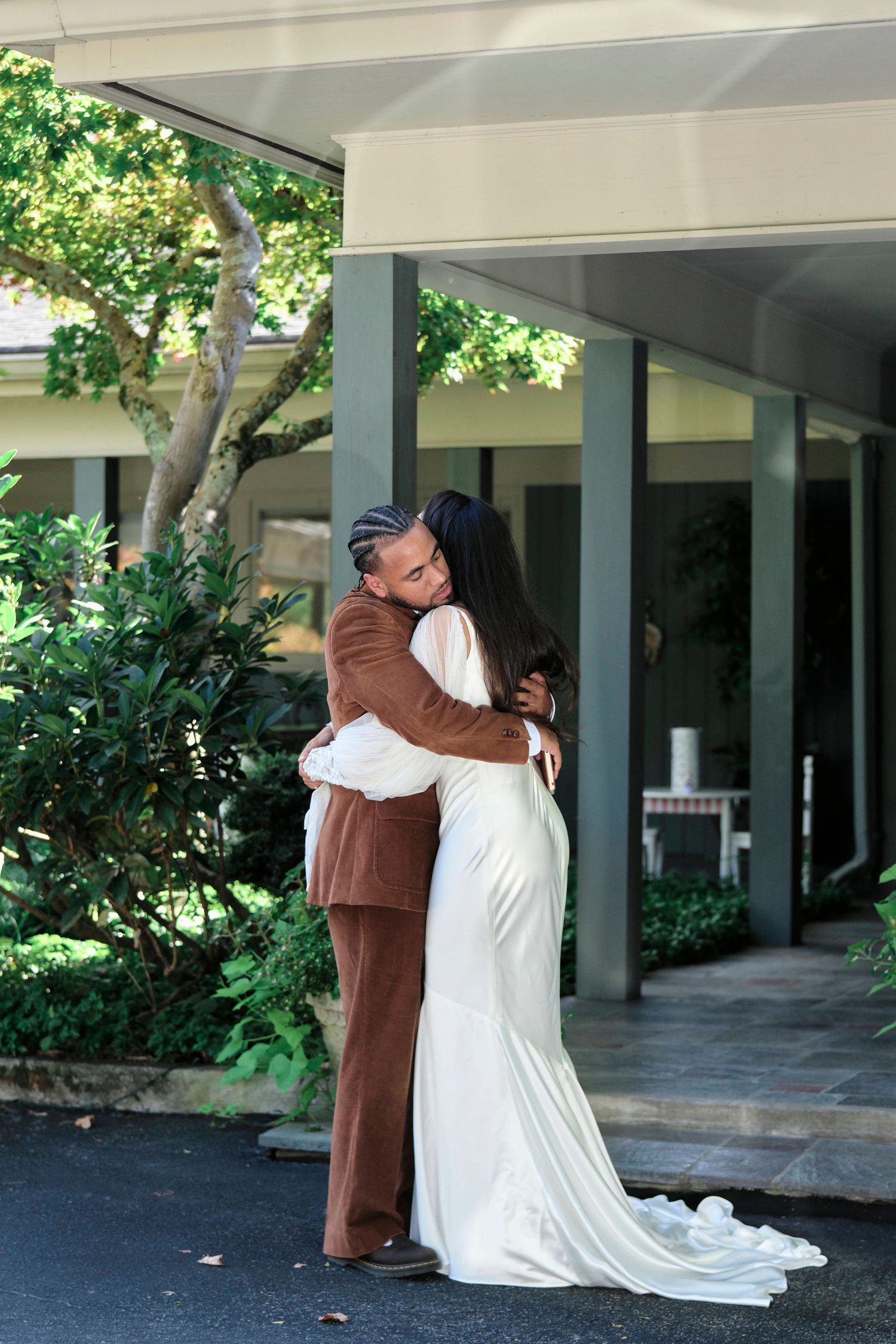 A couple in wedding attire share an intimate embrace on a covered porch.