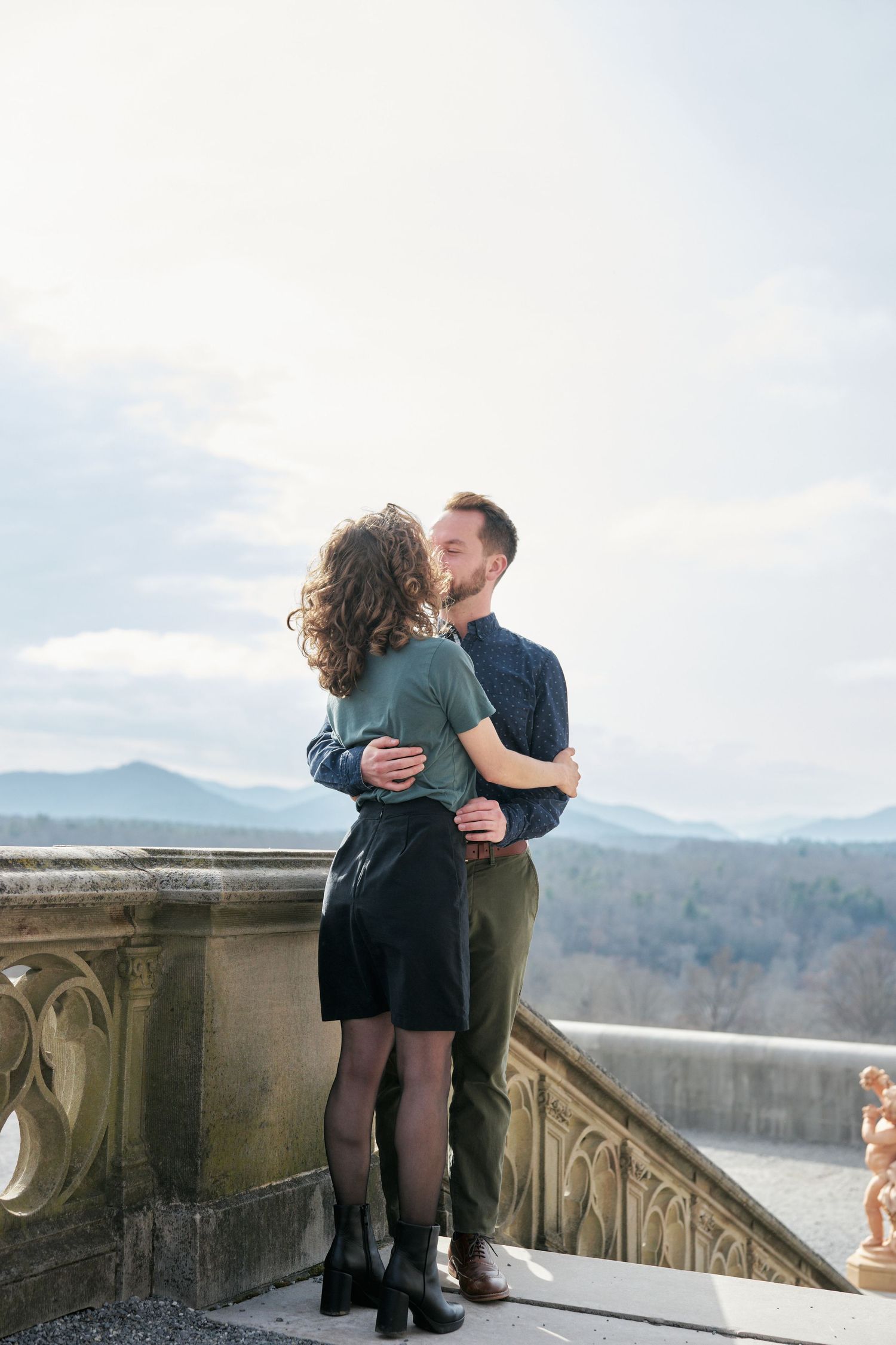 Couple kissing by the stairs at the Biltmore Estate with the mountains in the background.