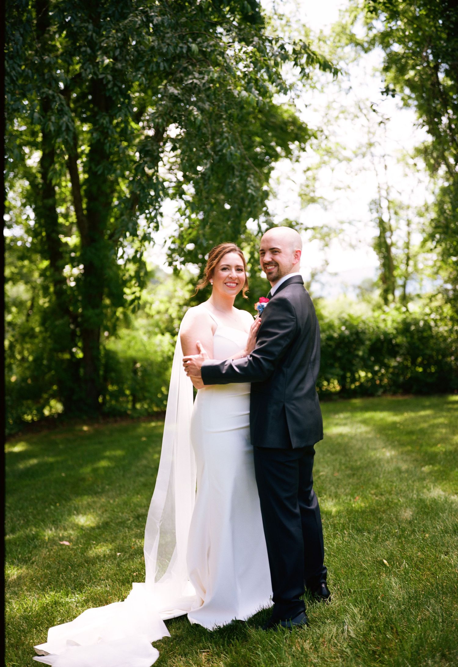 A couple shares an intimate moment on their wedding day in a sun-dappled garden setting.