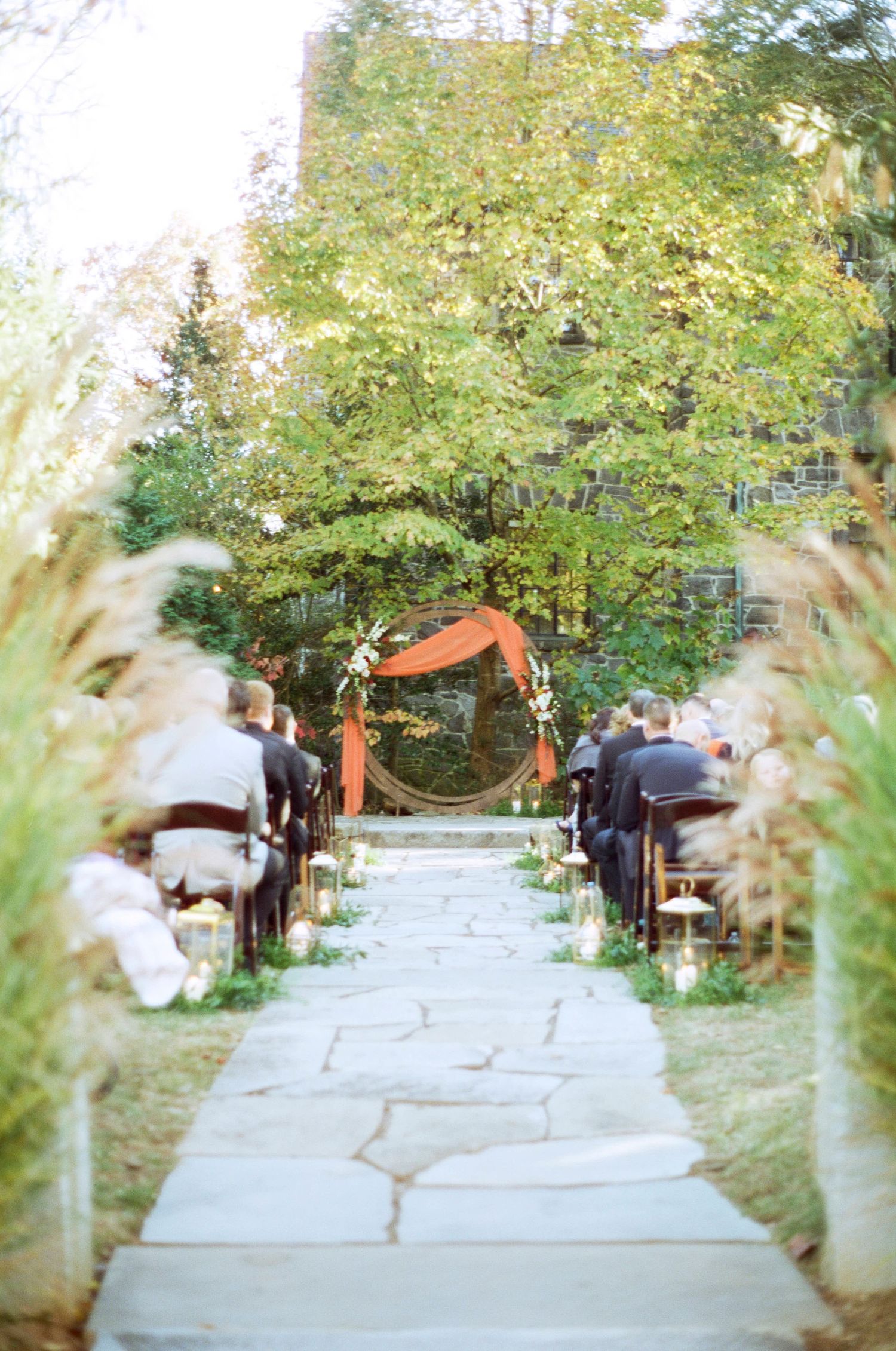 A stone pathway leads to a rustic wooden arch decorated for an outdoor autumn wedding ceremony.