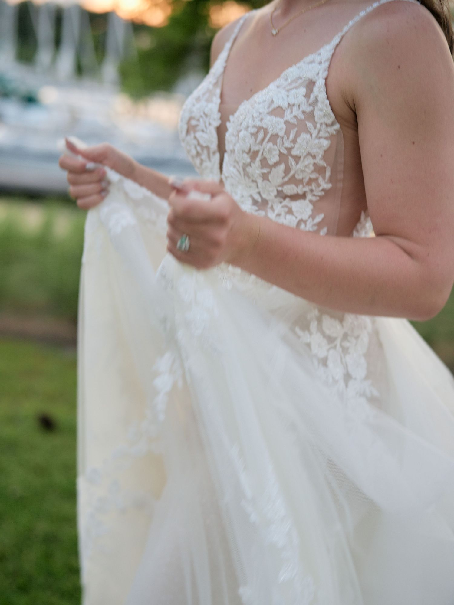 Close-up detail of a bride wearing a delicate lace bodice wedding dress while holding tulle fabric outdoors.