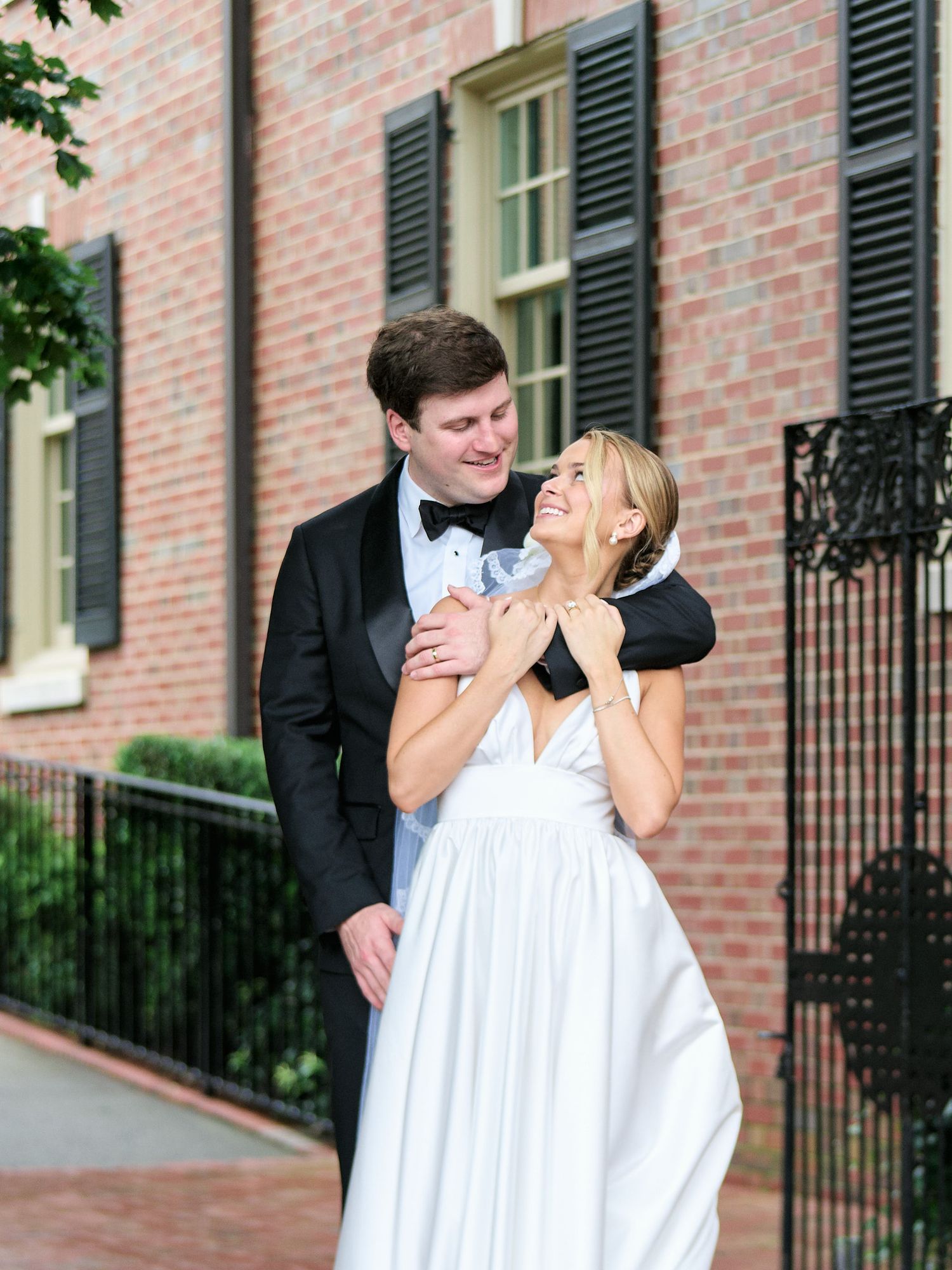 Joyful wedding moment captured as couple laughs together in front of brick building.
