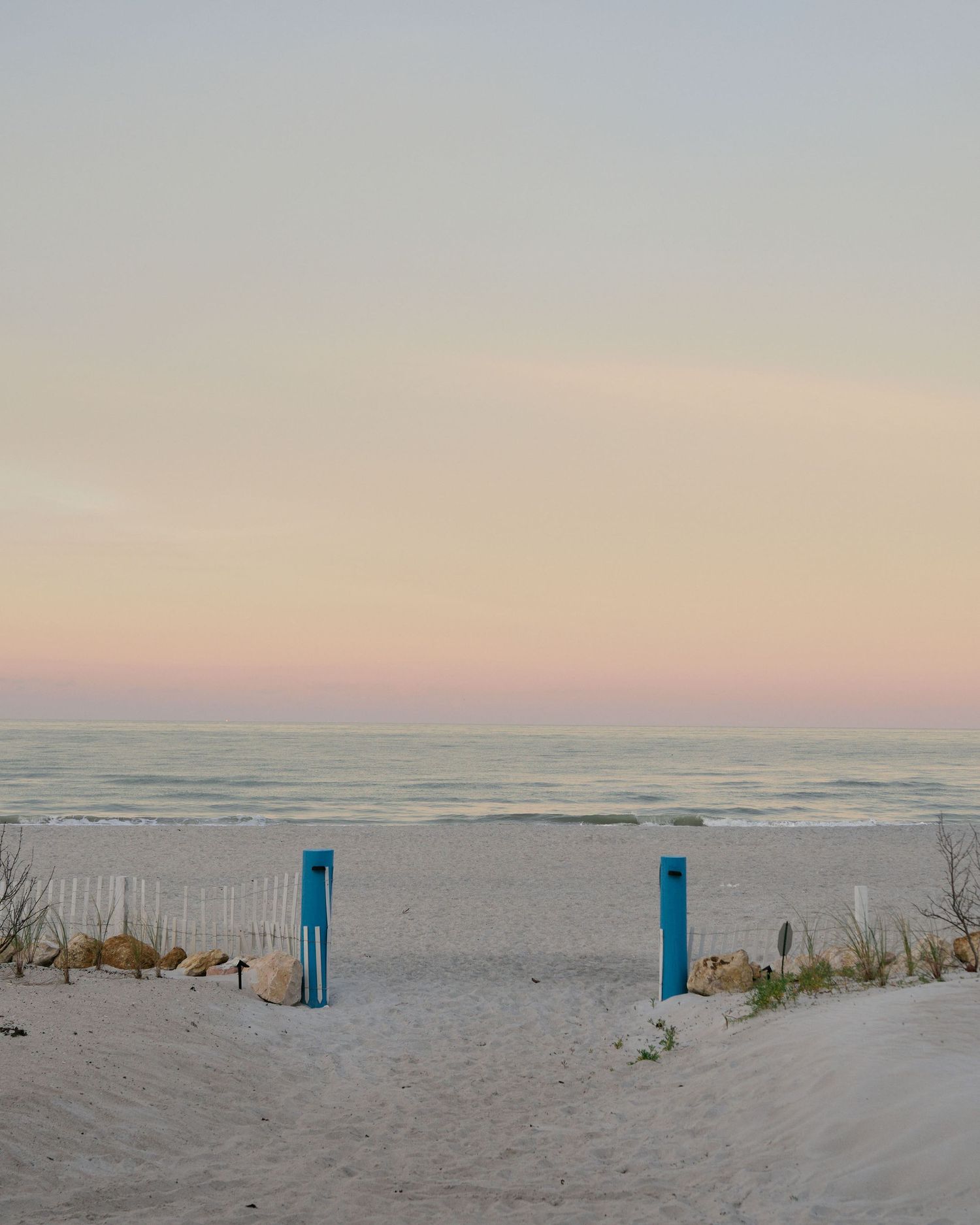A panoramic view of a sandy beach at sunset with blue posts marking the pathway through sand dunes.