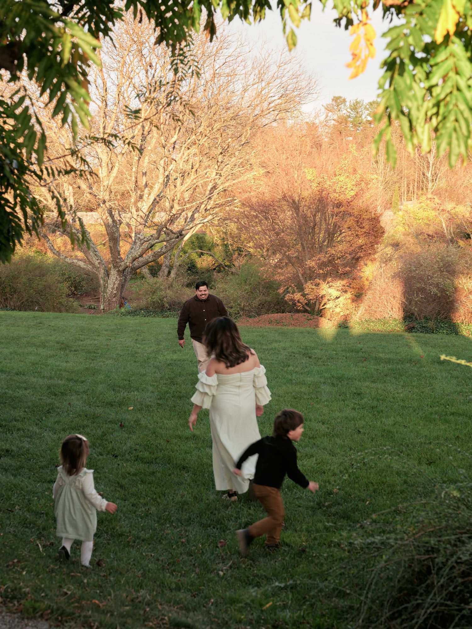 Family of four enjoying a golden hour walk on a lush green lawn surrounded by autumn trees.