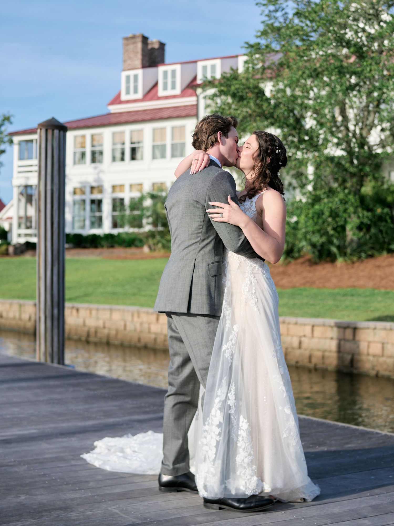 Romantic moment captured on a wooden dock with elegant mansion backdrop.