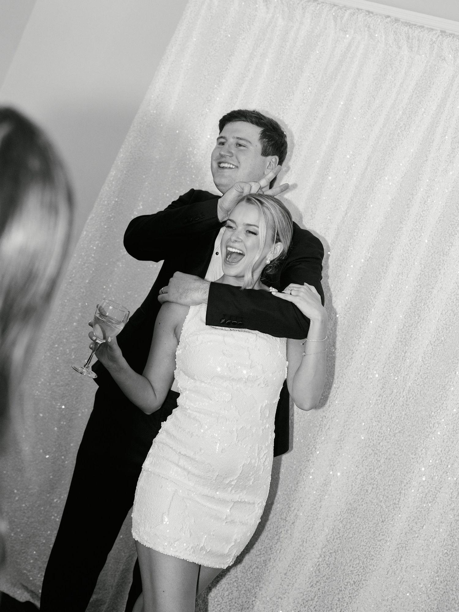 A couple shares a joyful moment laughing together at a wedding reception, with the bride wearing a short white dress.