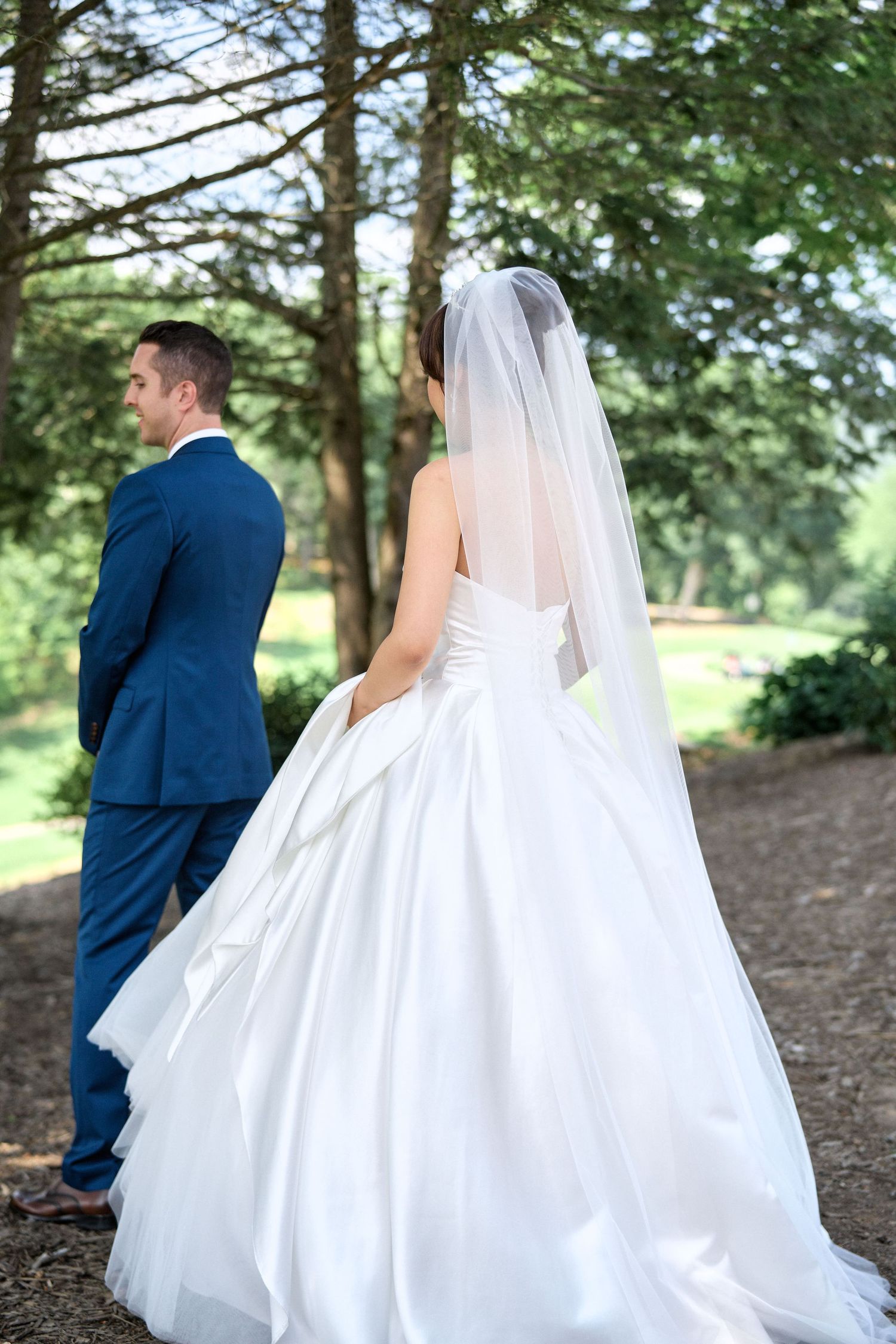 A bride and groom share a first look moment outdoors surrounded by pine trees.
