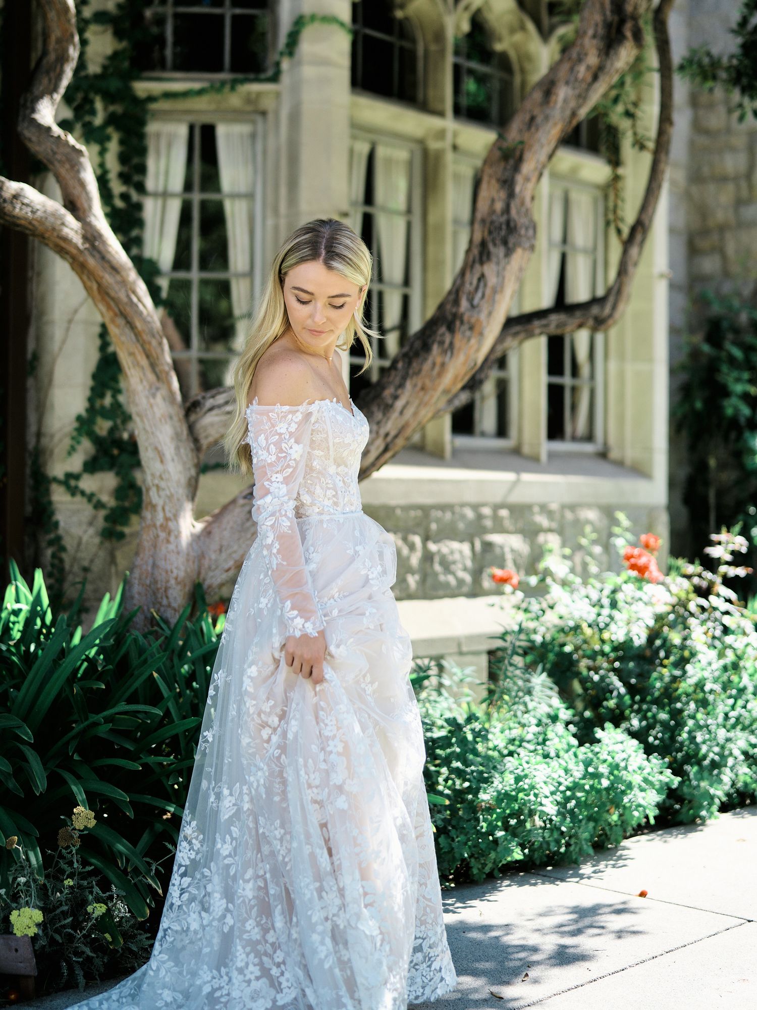 Ethereal lace wedding dress captured in garden setting with blooming flowers.