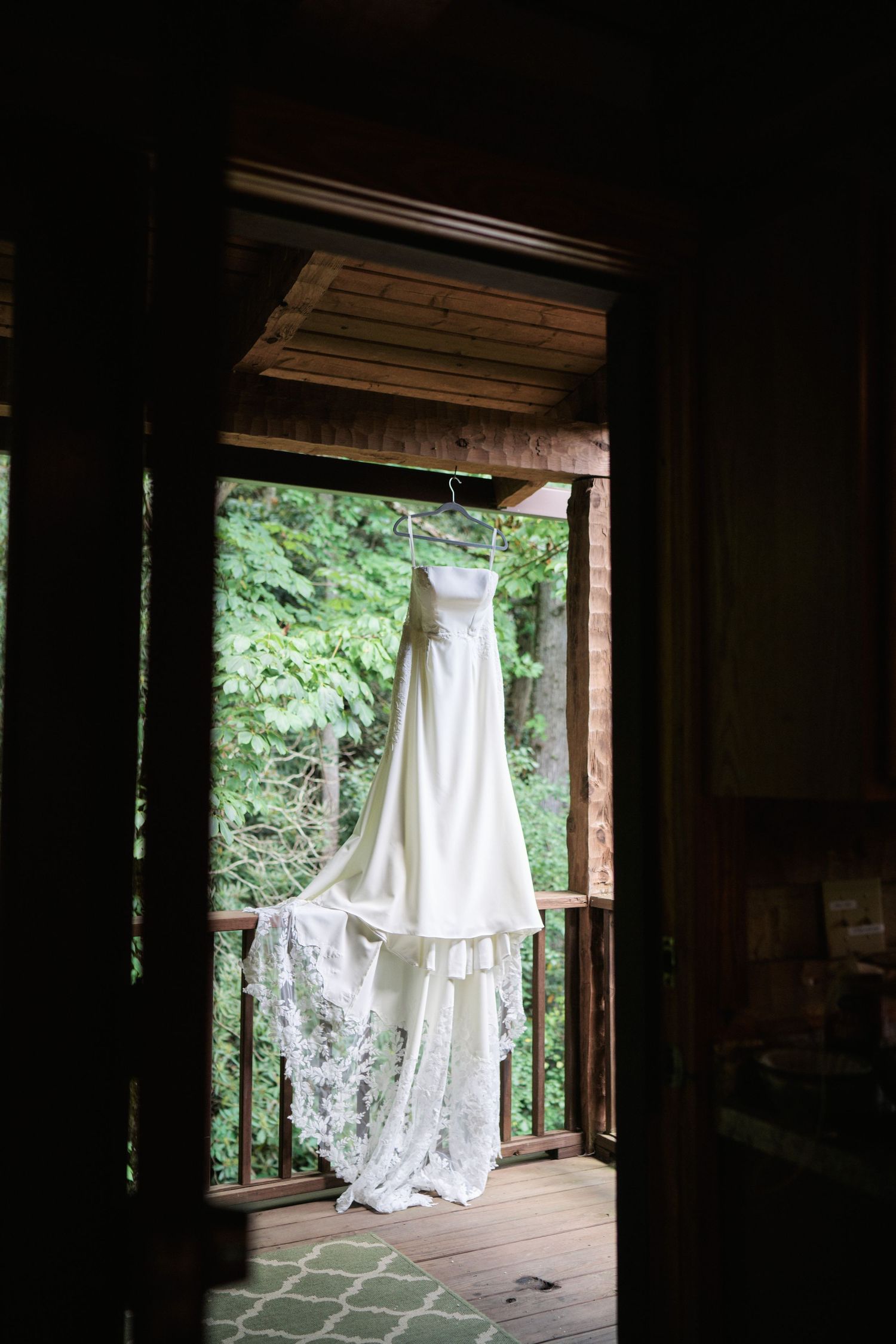 White wedding dress hanging on a rustic wooden porch surrounded by lush green trees.