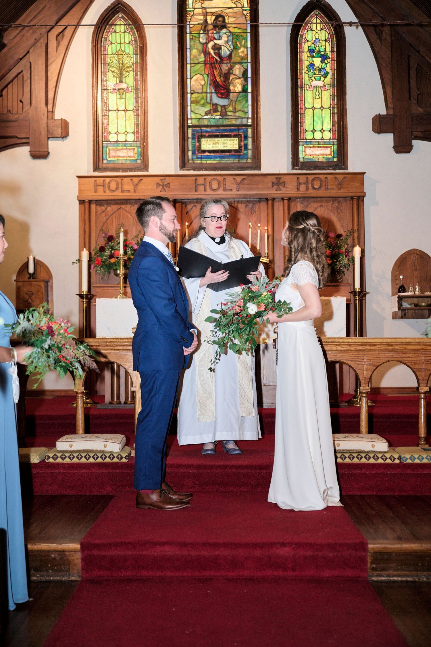 A wedding ceremony takes place in a church with beautiful stained glass windows and wooden beams overhead.