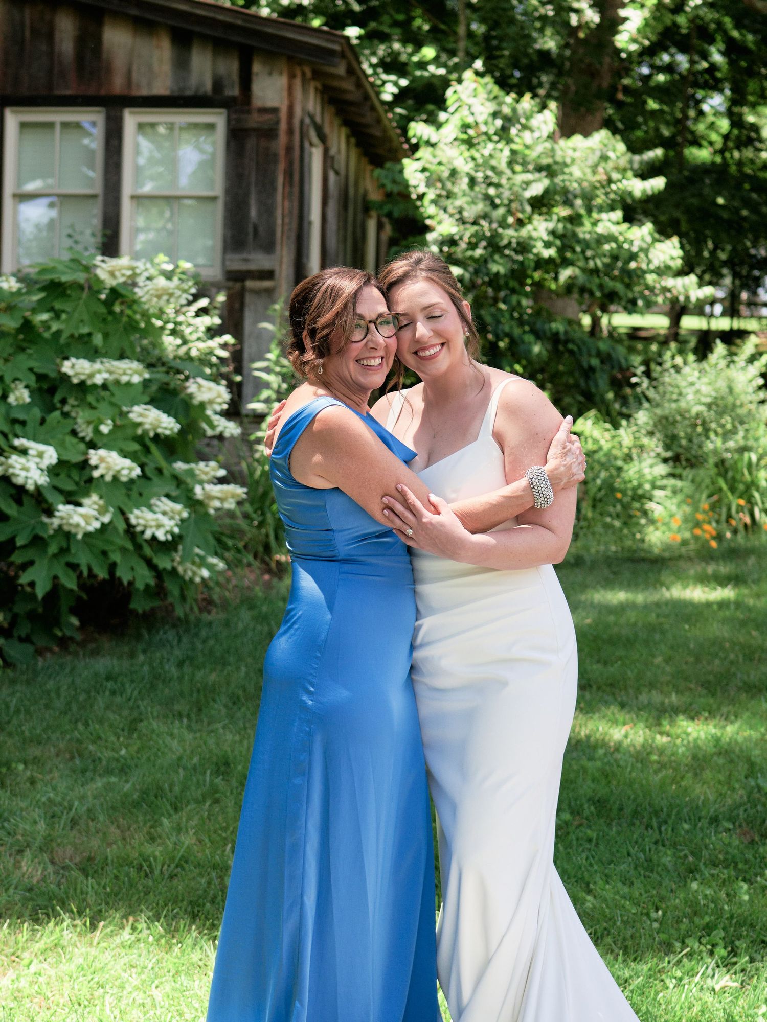 Two people embrace and smile while standing in front of a rustic wooden cabin.