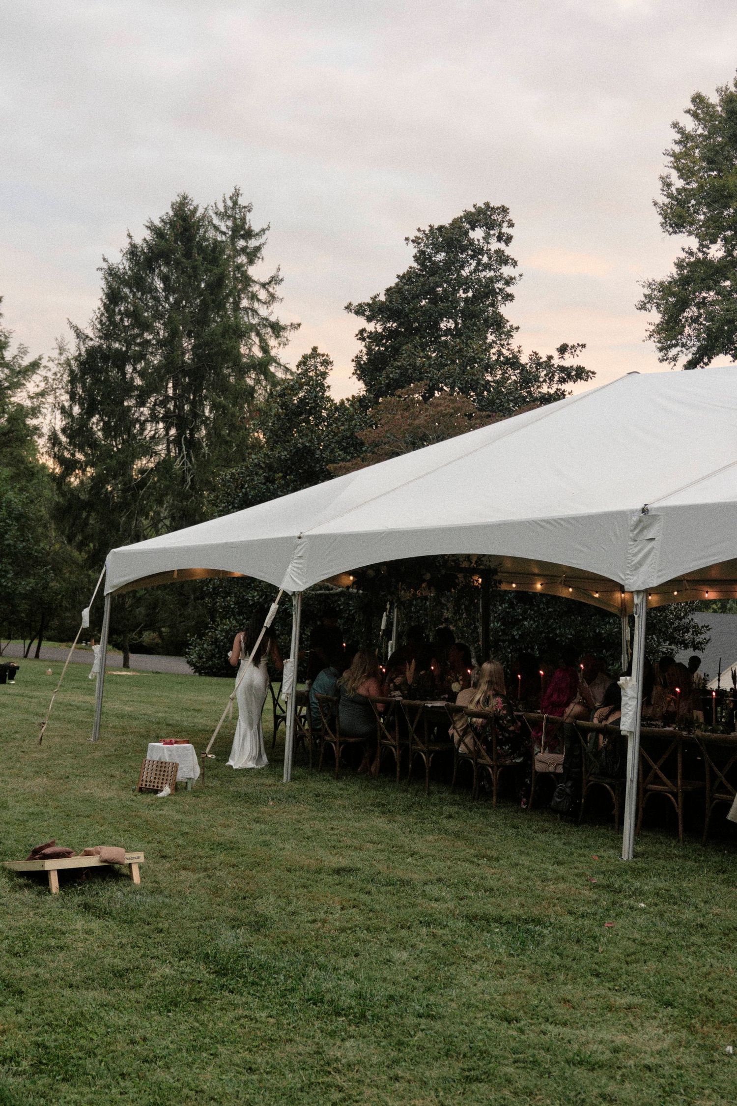A white wedding tent illuminated at dusk with guests seated inside.