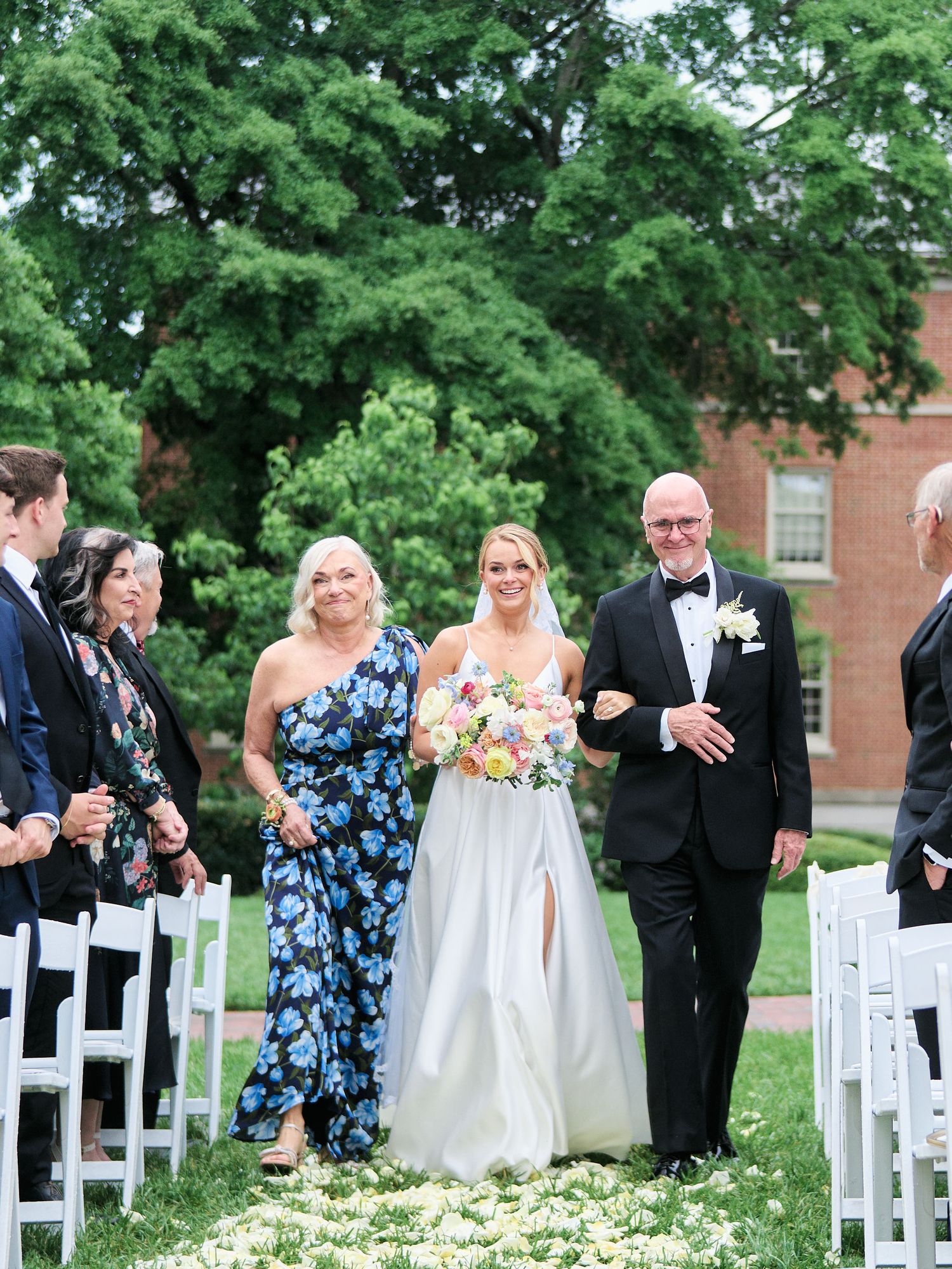 Wedding processional along flower-strewn aisle with elegant outdoor garden setting.