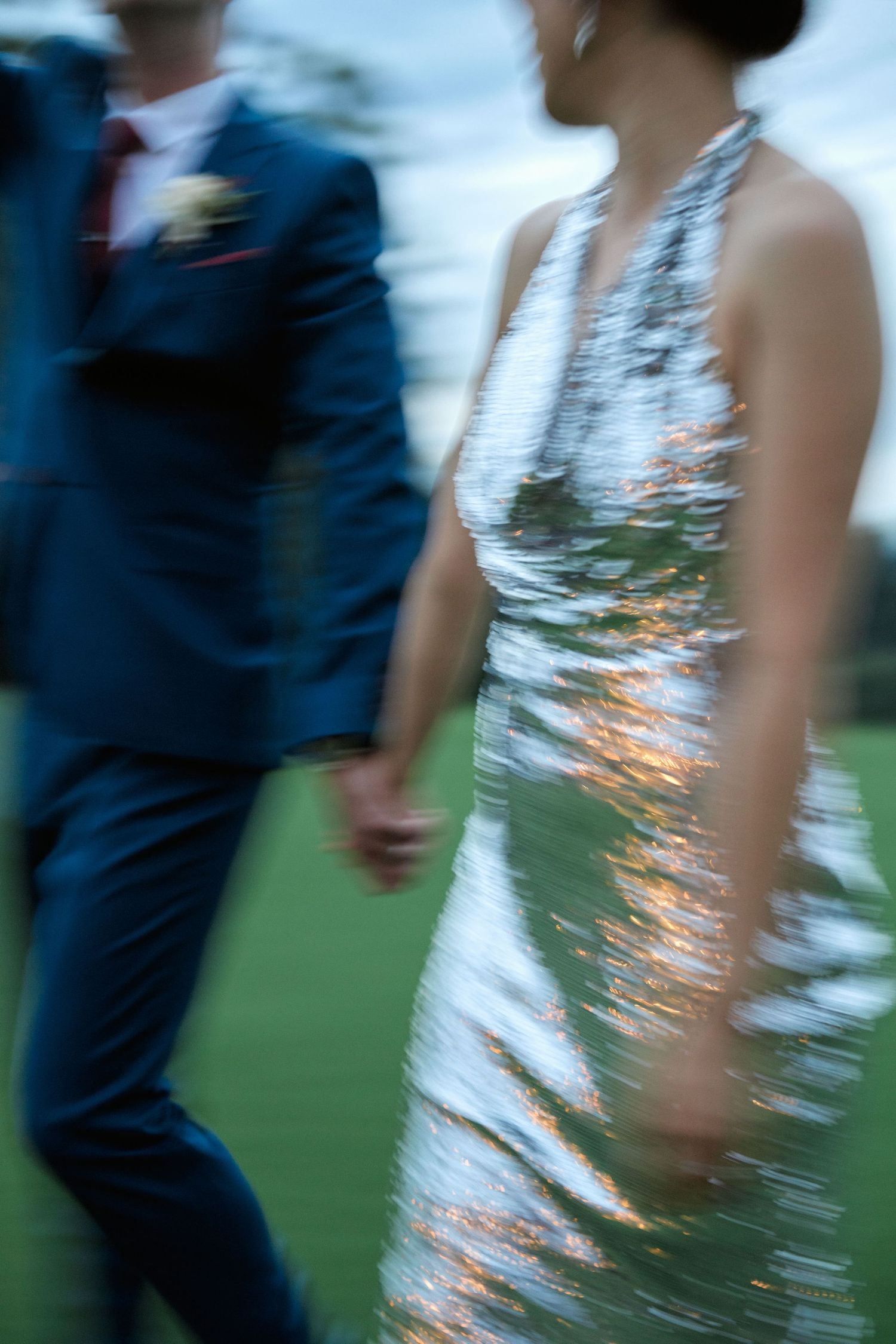 A motion-blurred artistic shot of a couple walking in formal attire on a golf course.