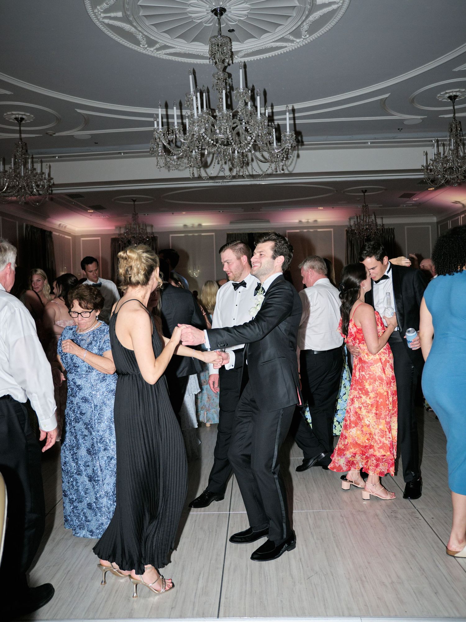 Wedding guests dancing beneath crystal chandeliers at an elegant evening reception.