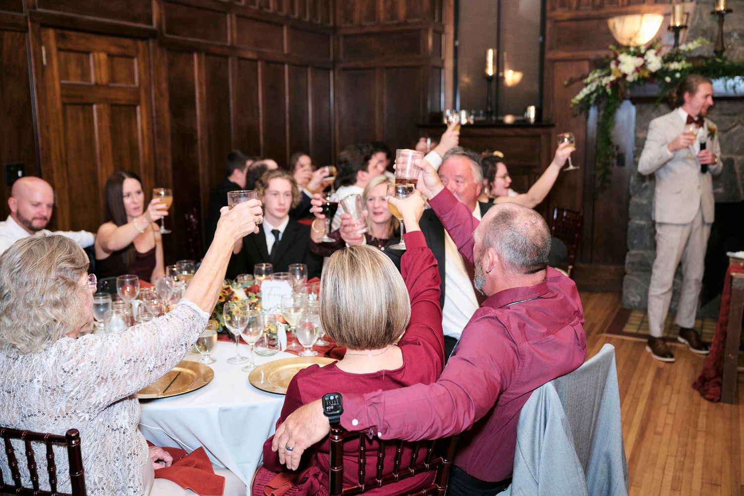 Wedding guests raising glasses in celebration during a toast at reception dinner.
