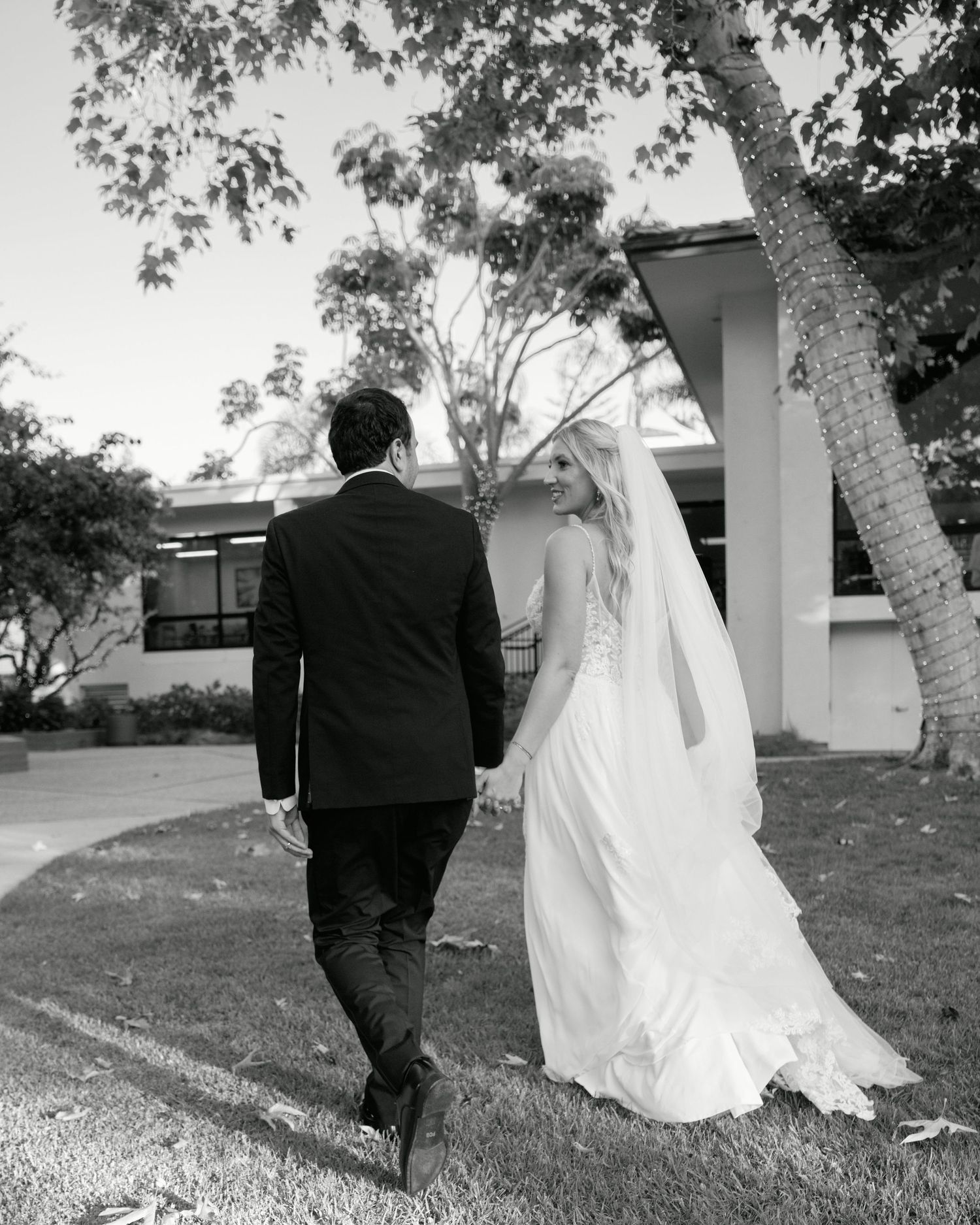 A black and white photo of a couple walking away on their wedding day through a garden setting.