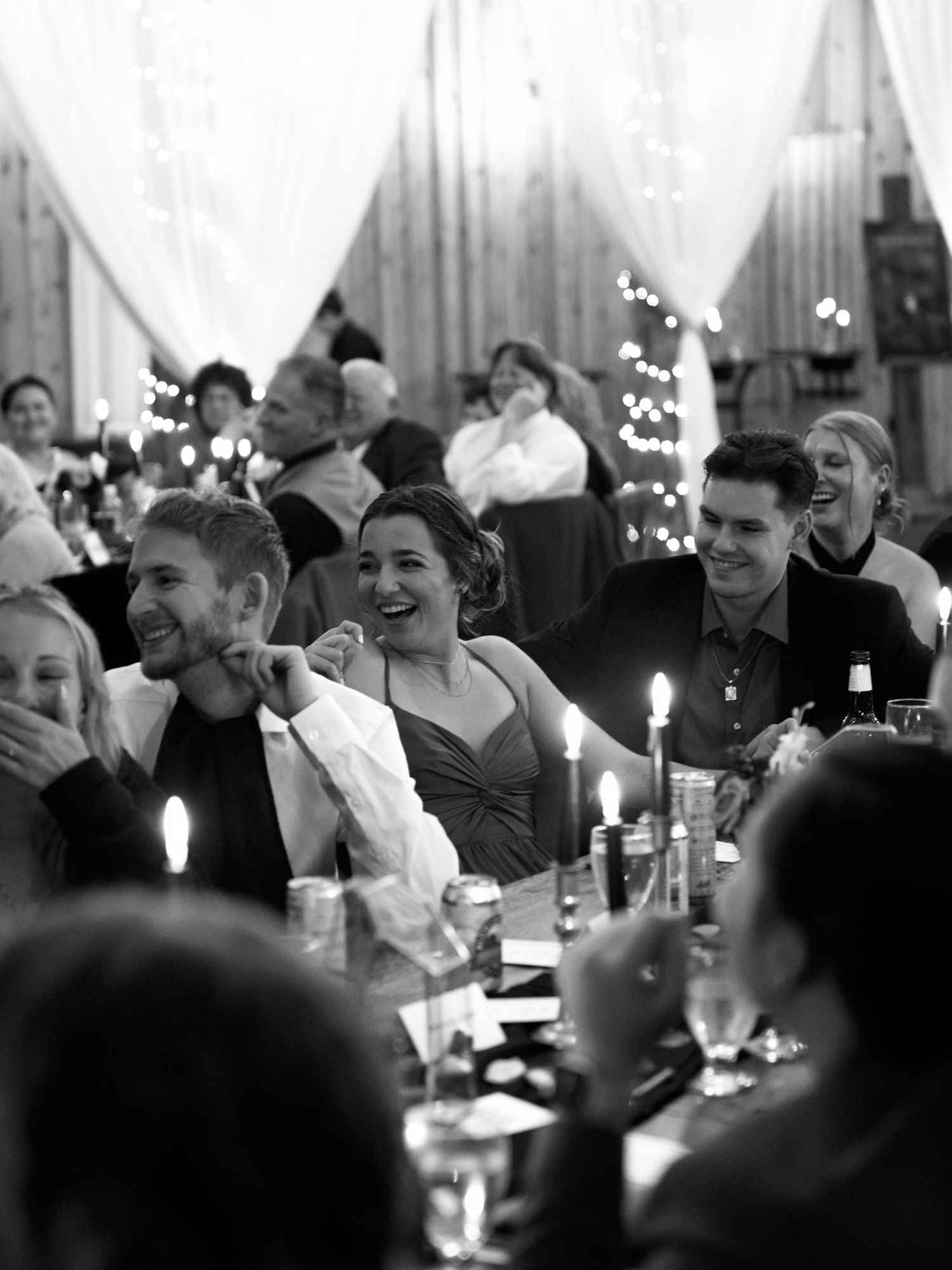 Wedding guests enjoying a candlelit reception dinner with warm ambient lighting.