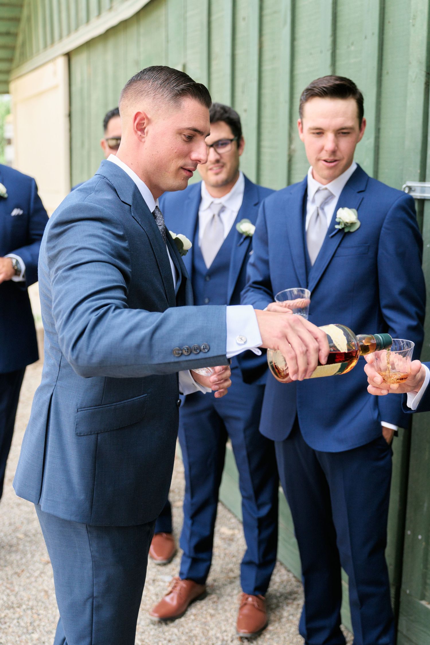 Groomsmen in blue suits pour champagne while celebrating outdoors.