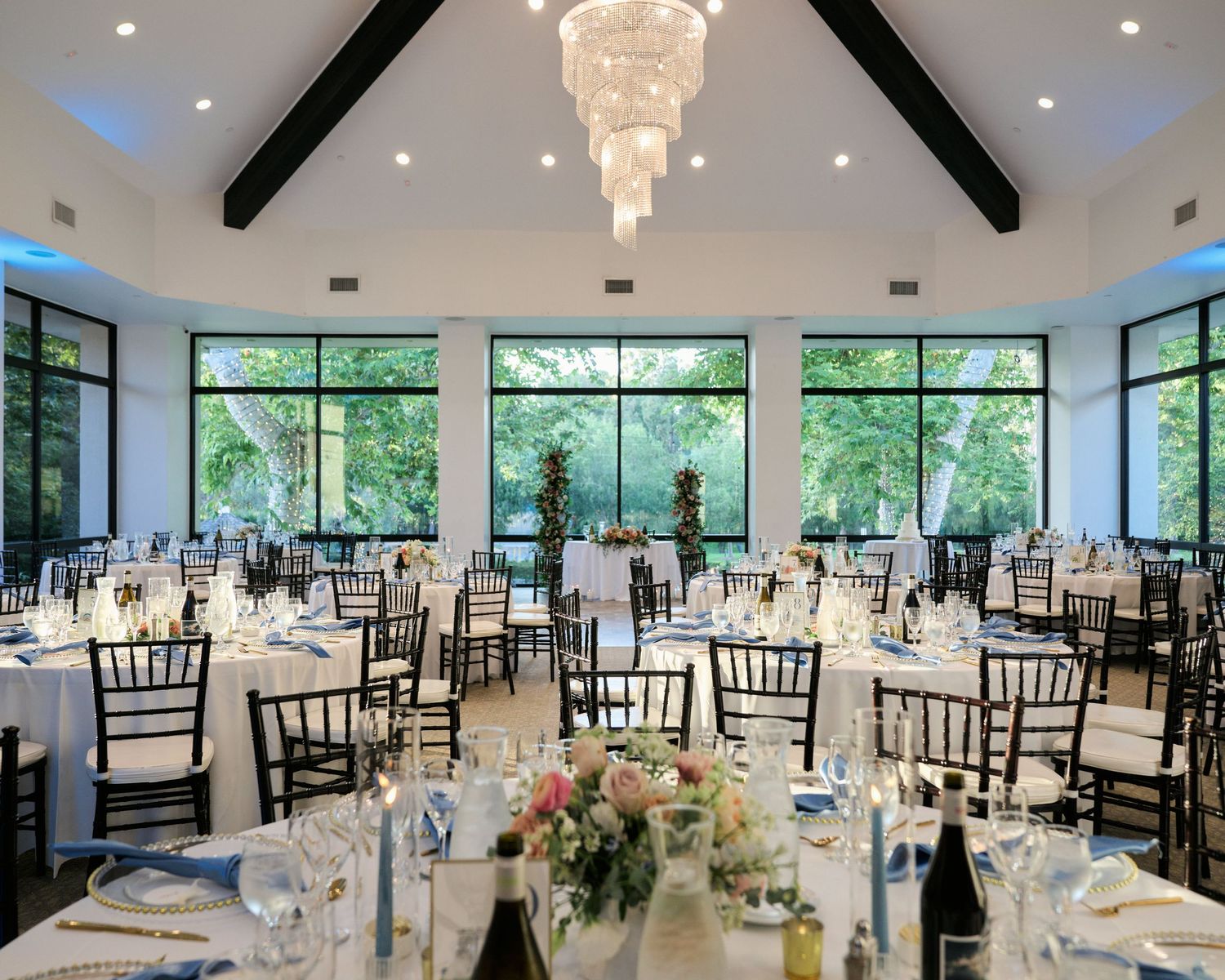 A modern wedding reception venue with high ceilings, crystal chandeliers, and floor-to-ceiling windows.