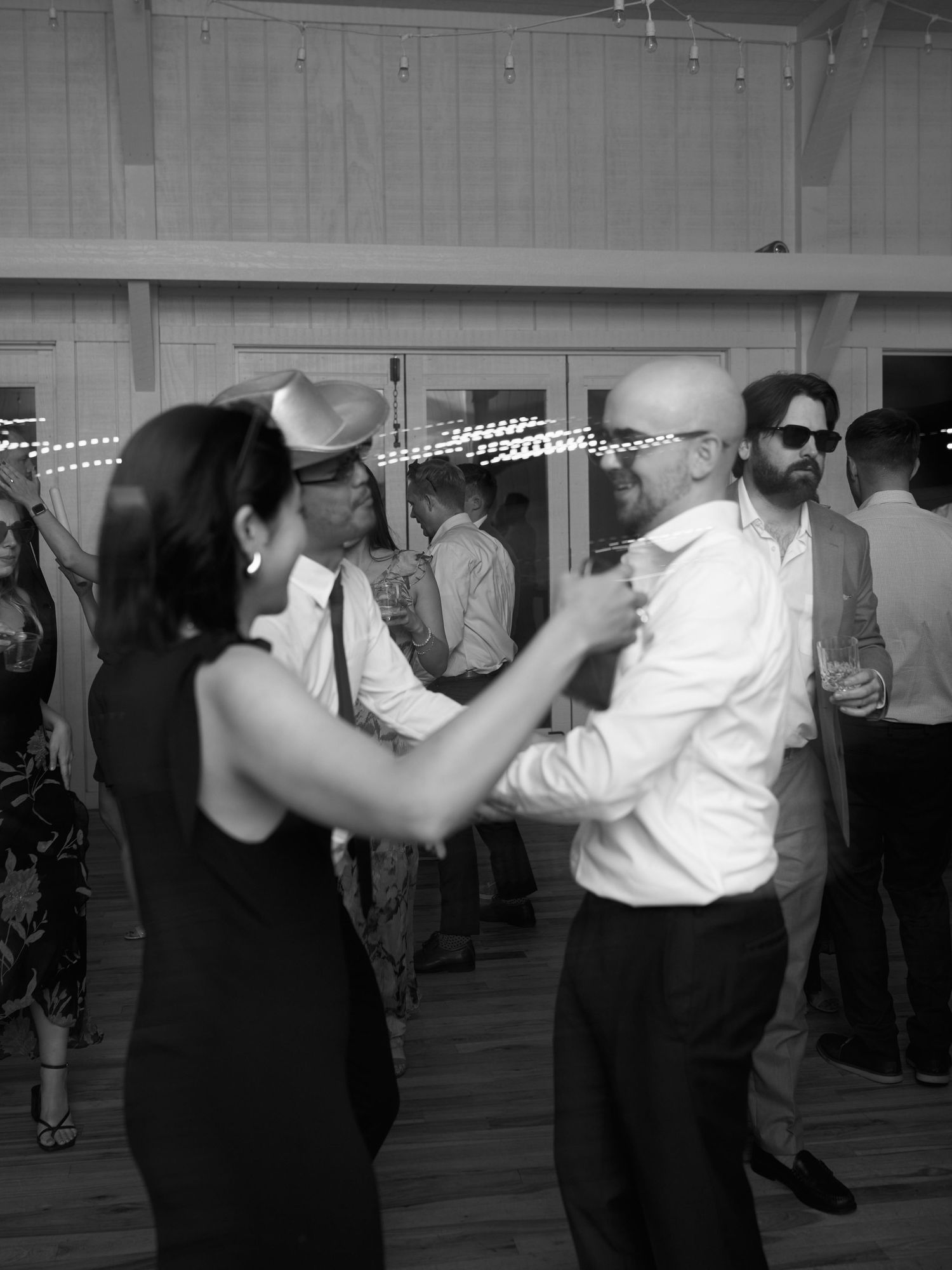 Couples dancing together at a lively party with decorative lights in the background.