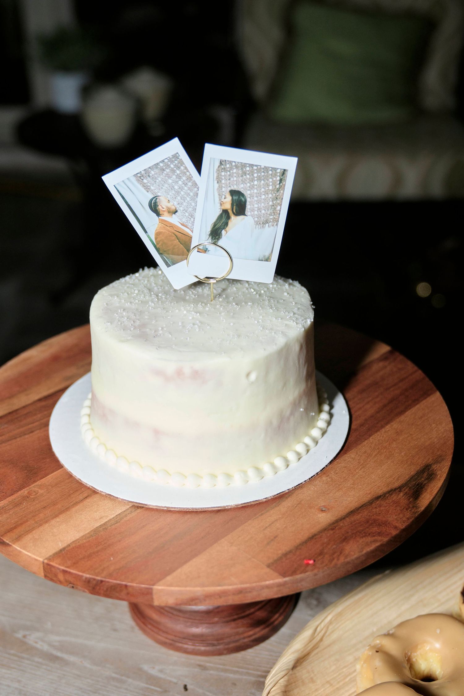 A simple white wedding cake decorated with Polaroid photos on a wooden cake stand.