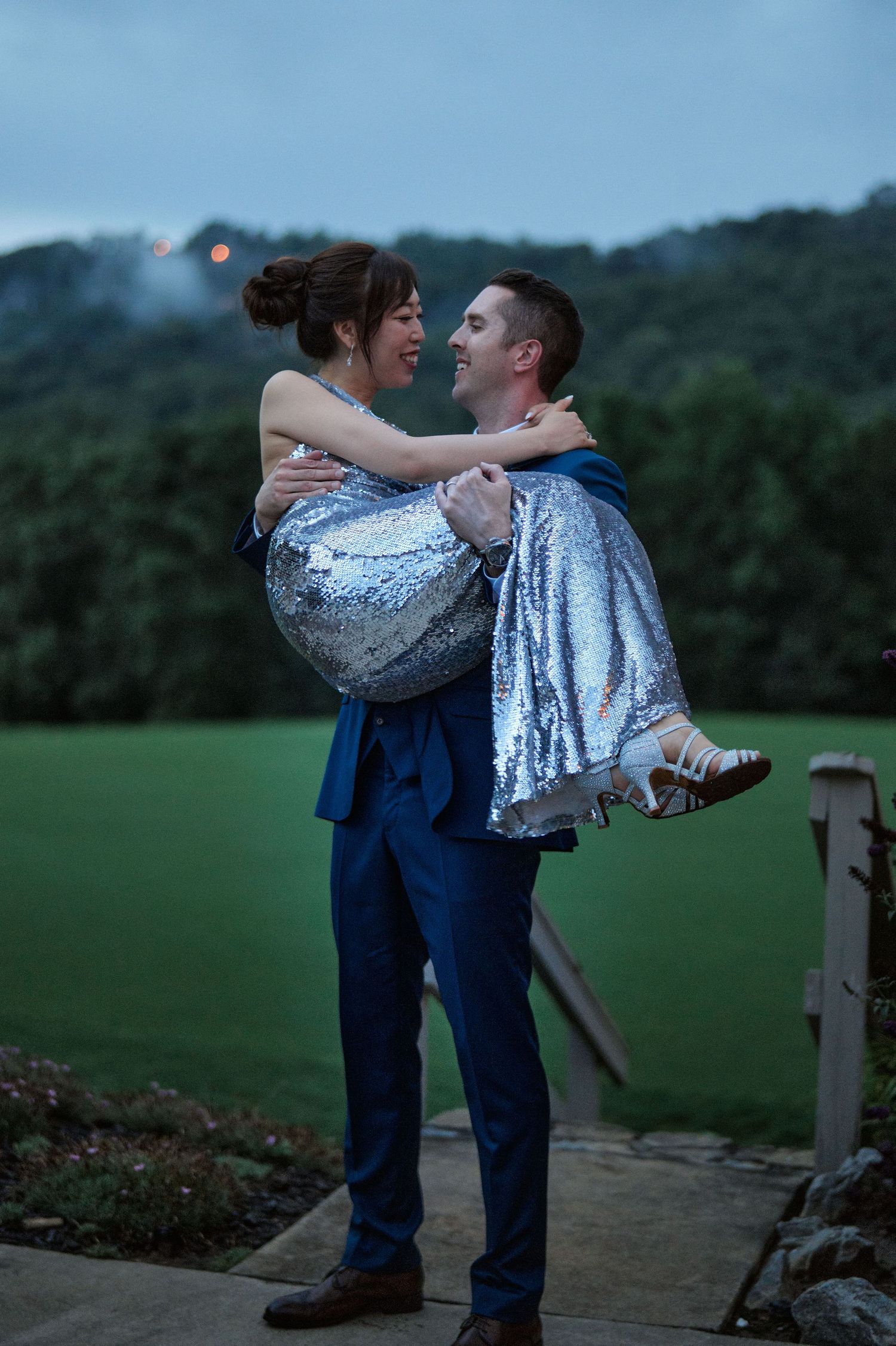 A joyful moment captured as the groom lifts his bride on an outdoor platform at dusk.