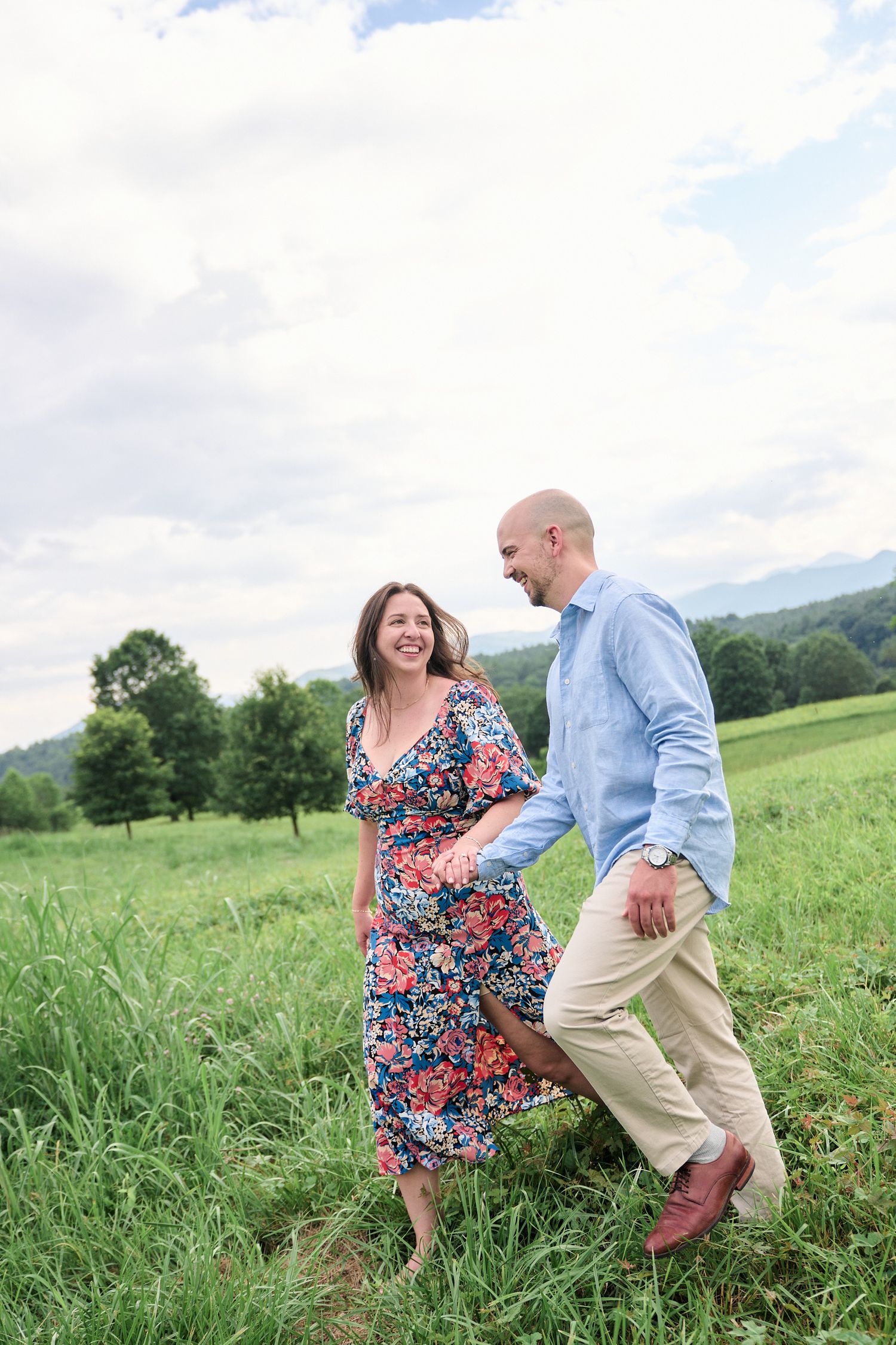 Joyful couple walking and laughing together in a green mountain field.