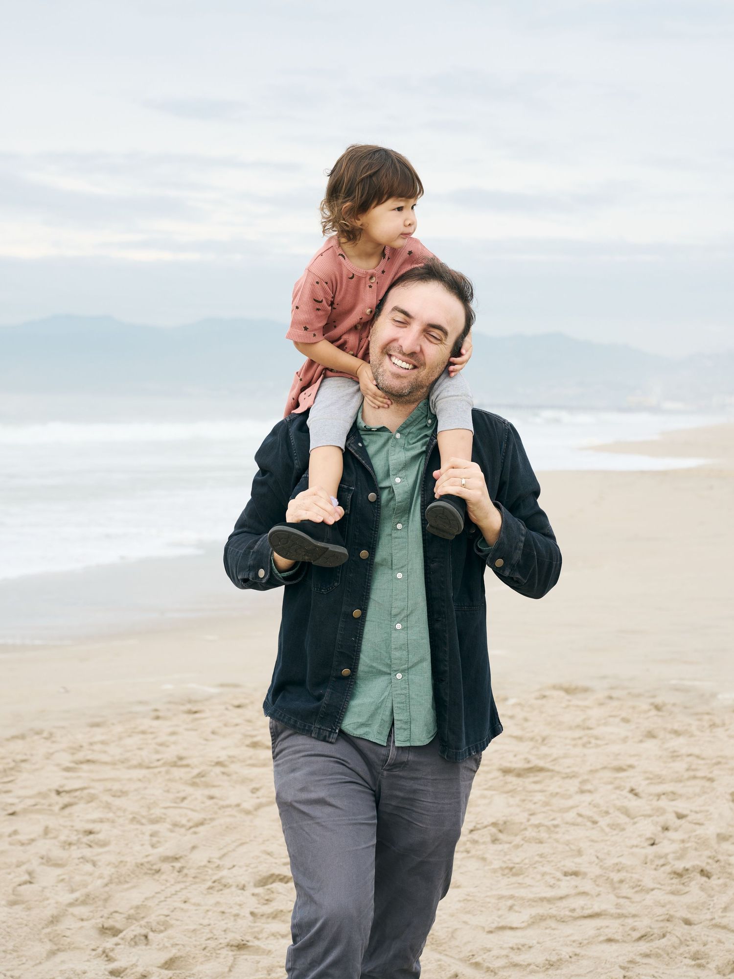 Two people enjoying a sunny day together on a sandy beach with mountains visible in the background.