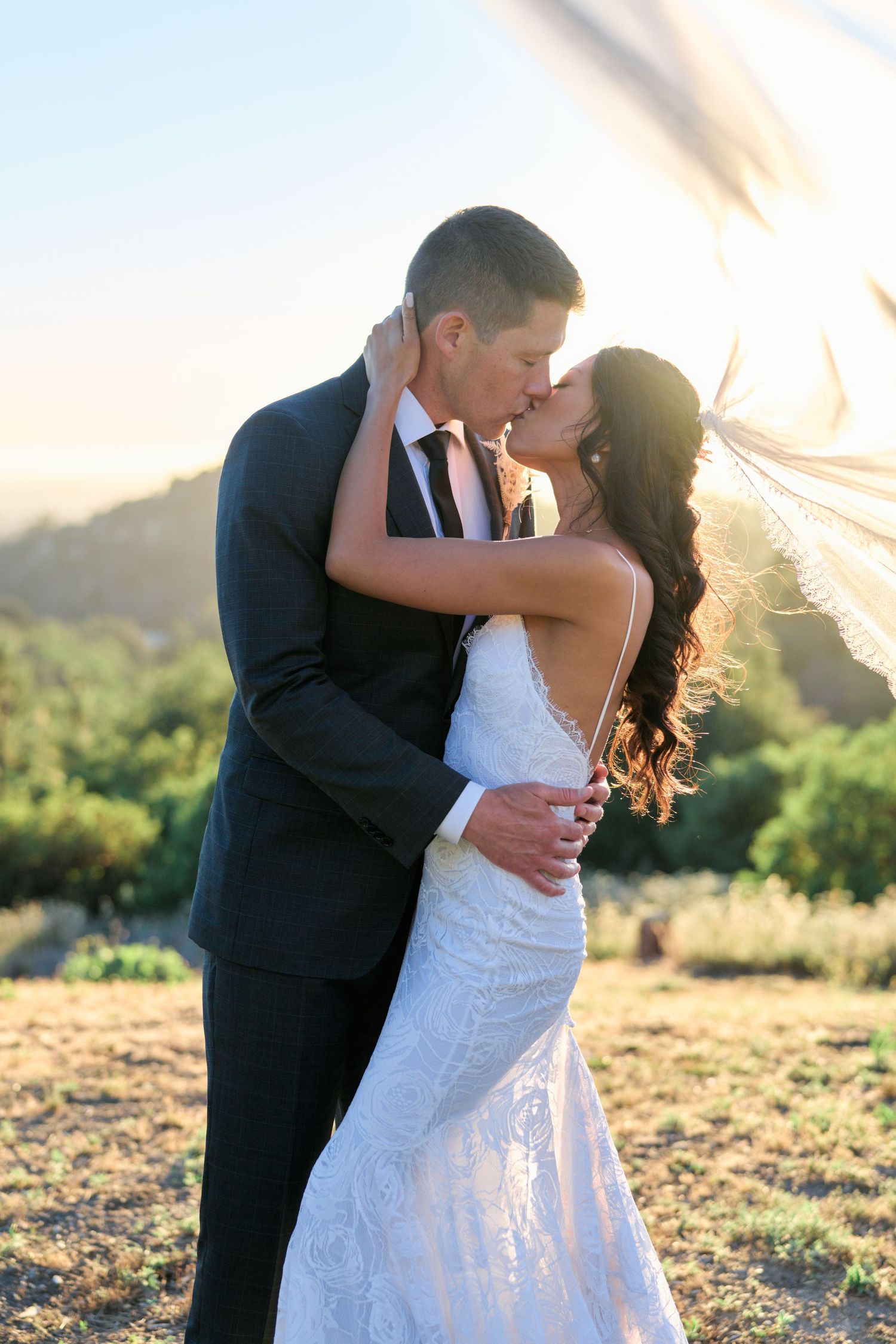 A romantic wedding embrace captured during golden hour with mountains in the background.