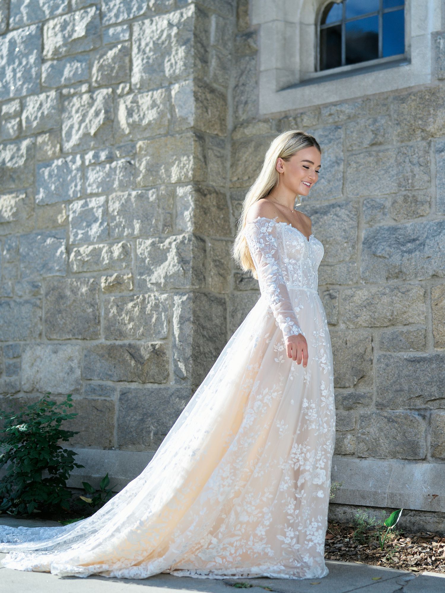Elegant lace wedding gown with long sleeves photographed against stone church wall.