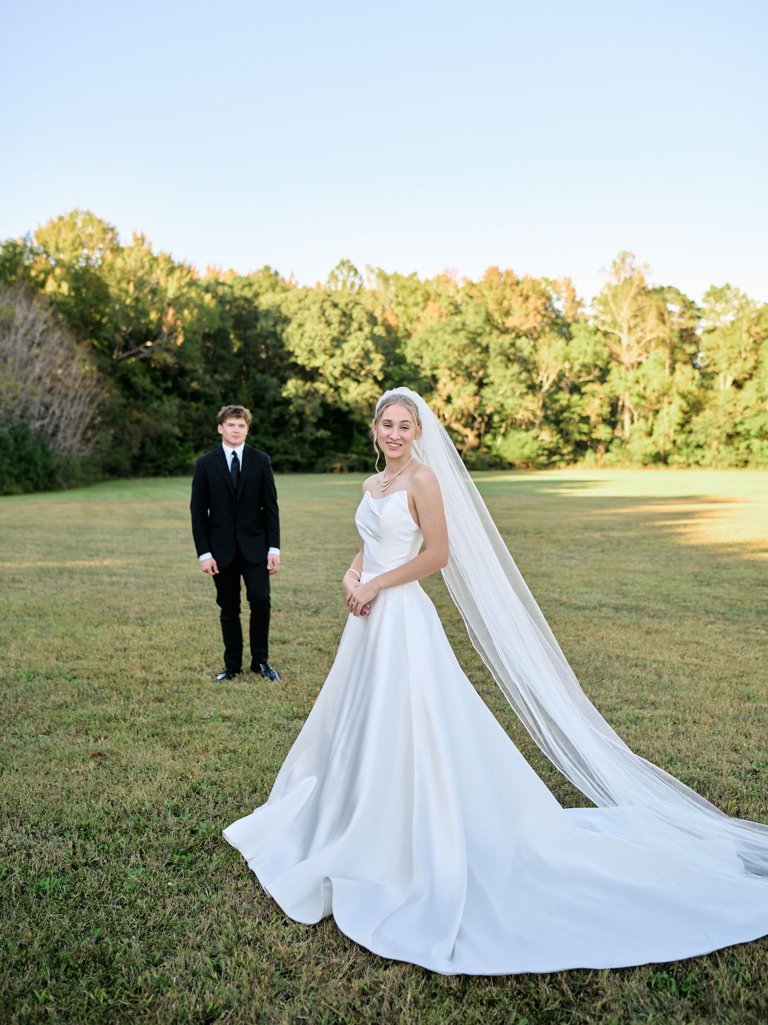 A series of wedding photos showing a bride in a flowing white dress with a long veil standing in a sunny field.