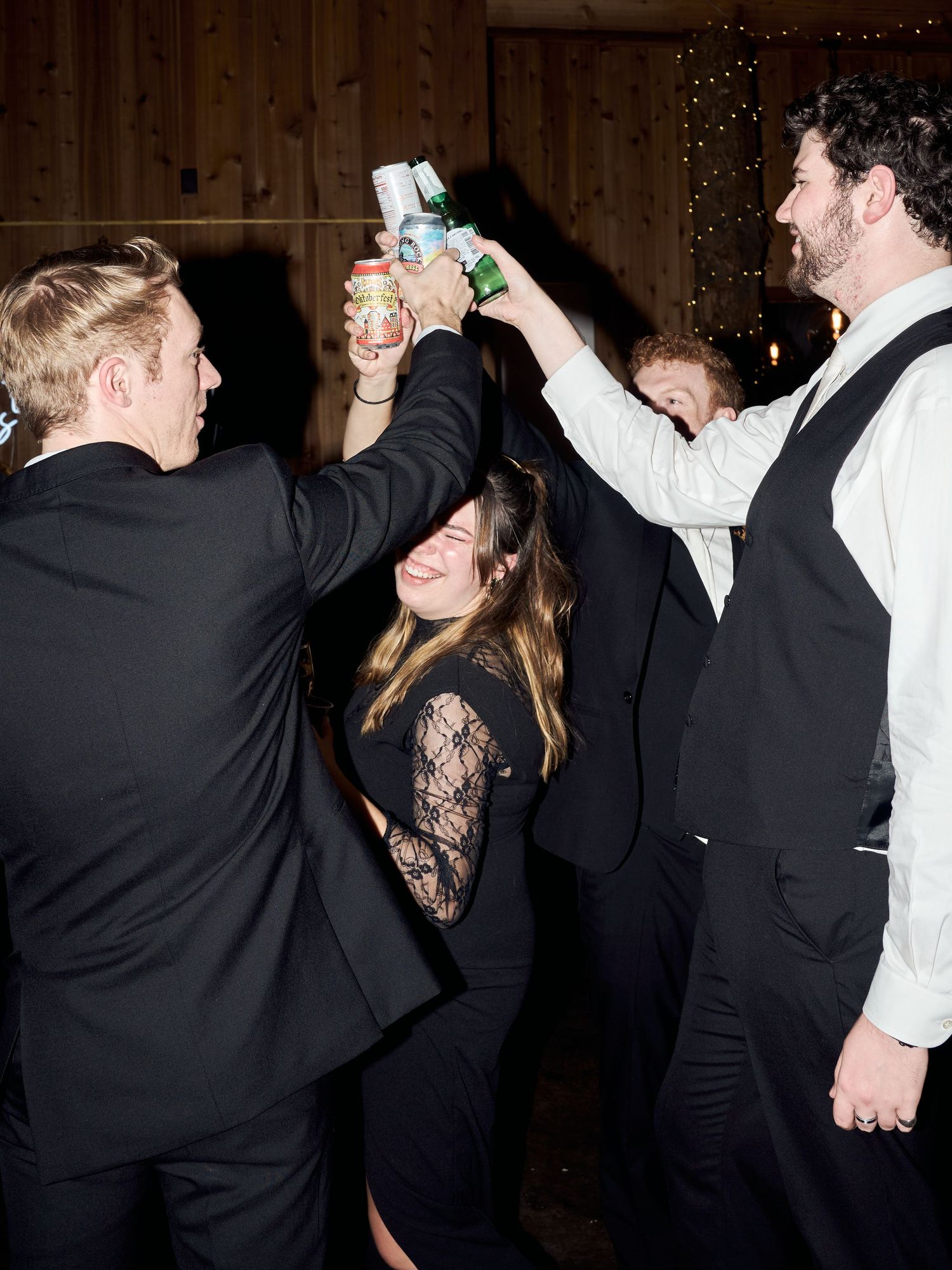 Party guests raise their drinks in celebration at a rustic venue with twinkling lights.