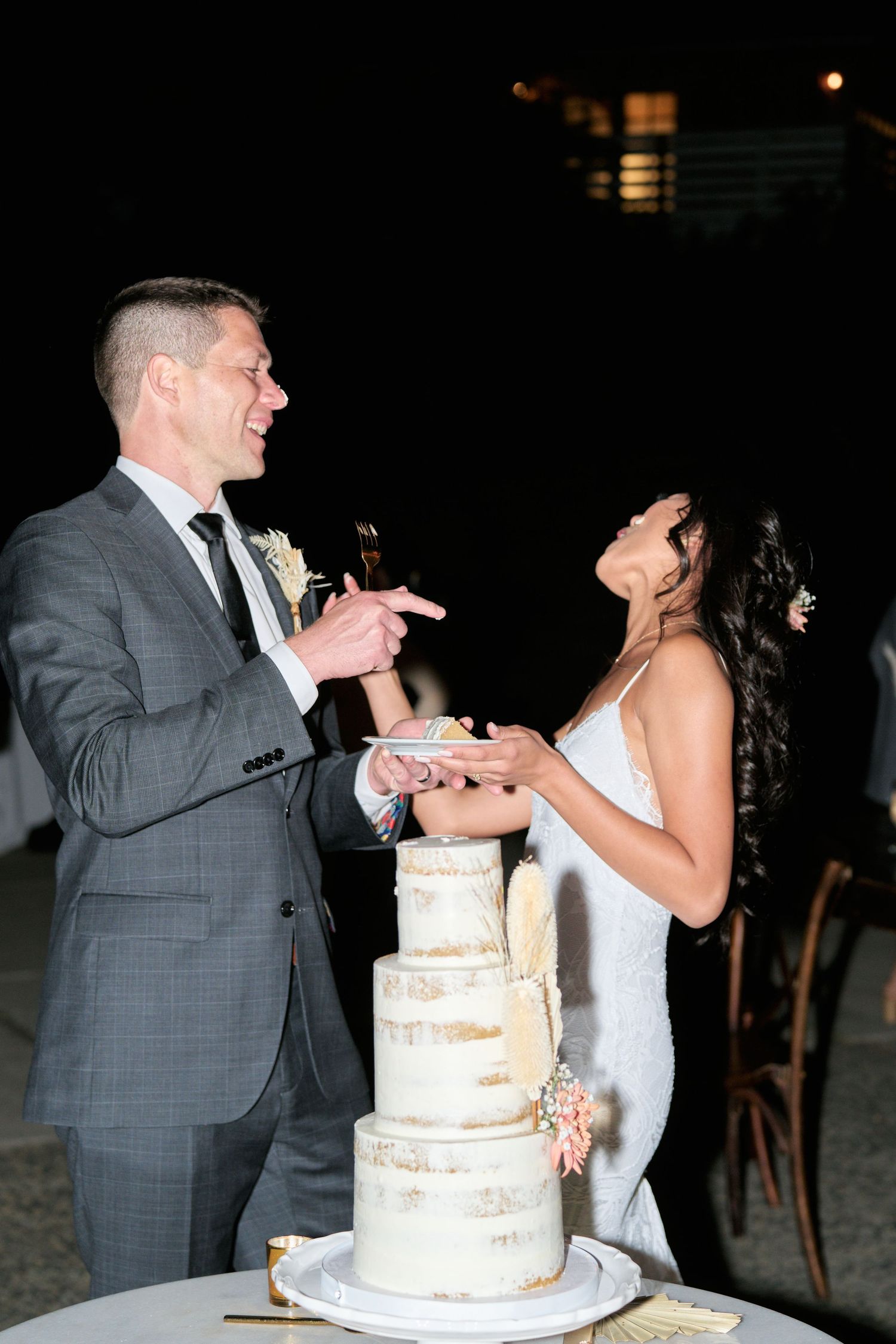 Bride and groom laugh while sharing cake at their wedding reception.