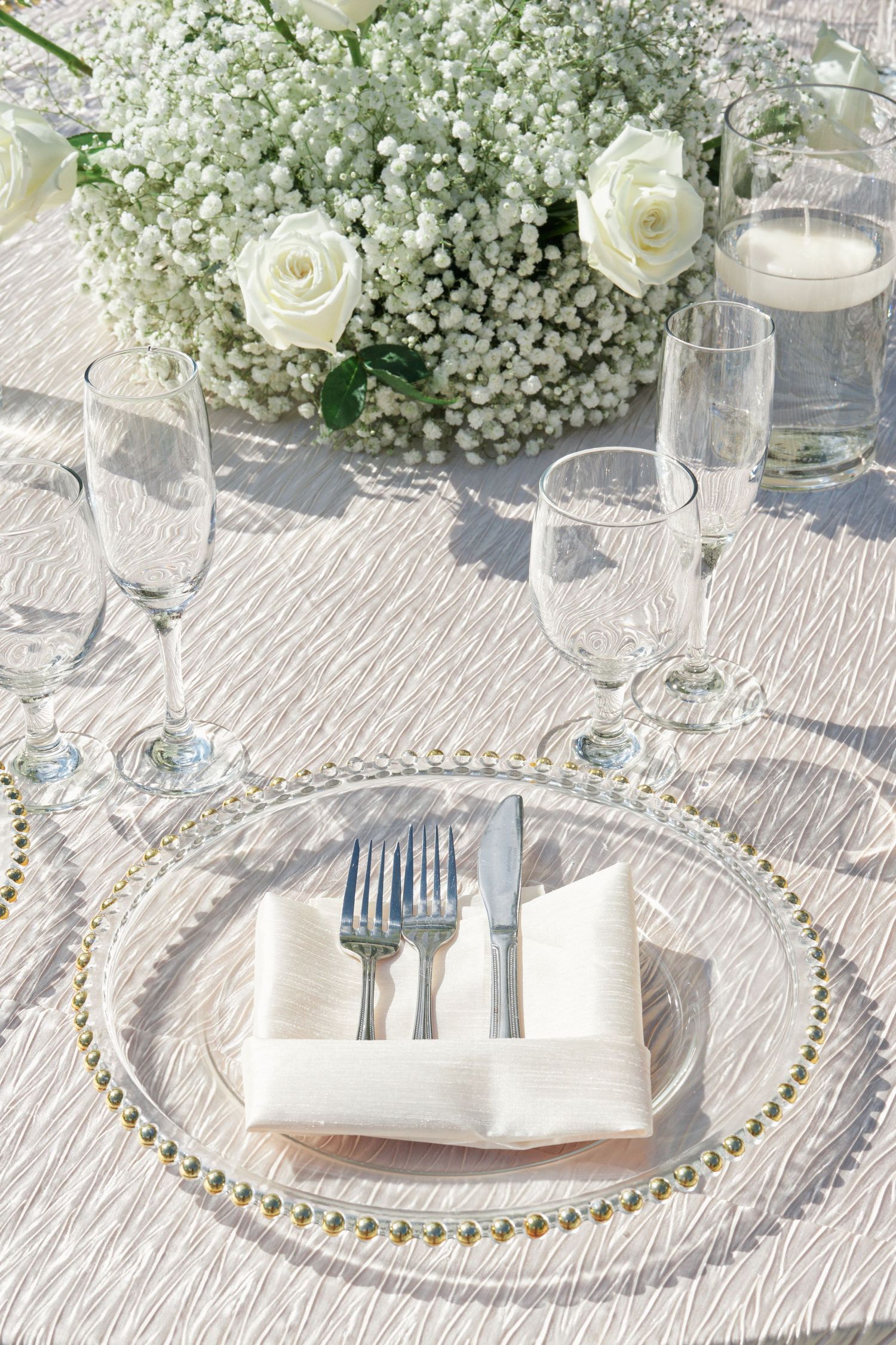 Elegant place setting with pearl-rimmed charger plate and white roses centerpiece.