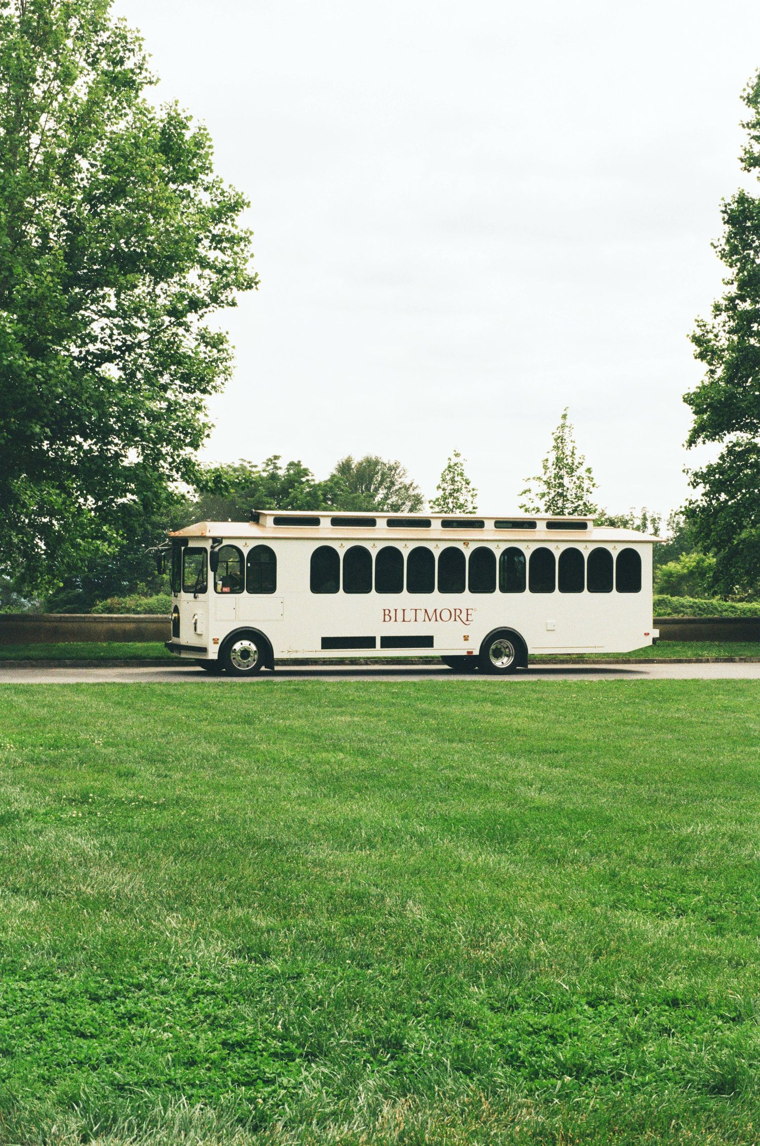White vintage-style trolley bus parked on green lawn in a park setting.