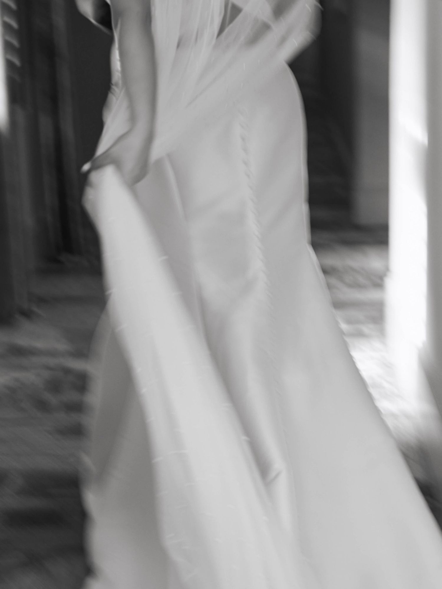 A black and white motion blur photograph of a person dancing in flowing white fabric creating ethereal movement.
