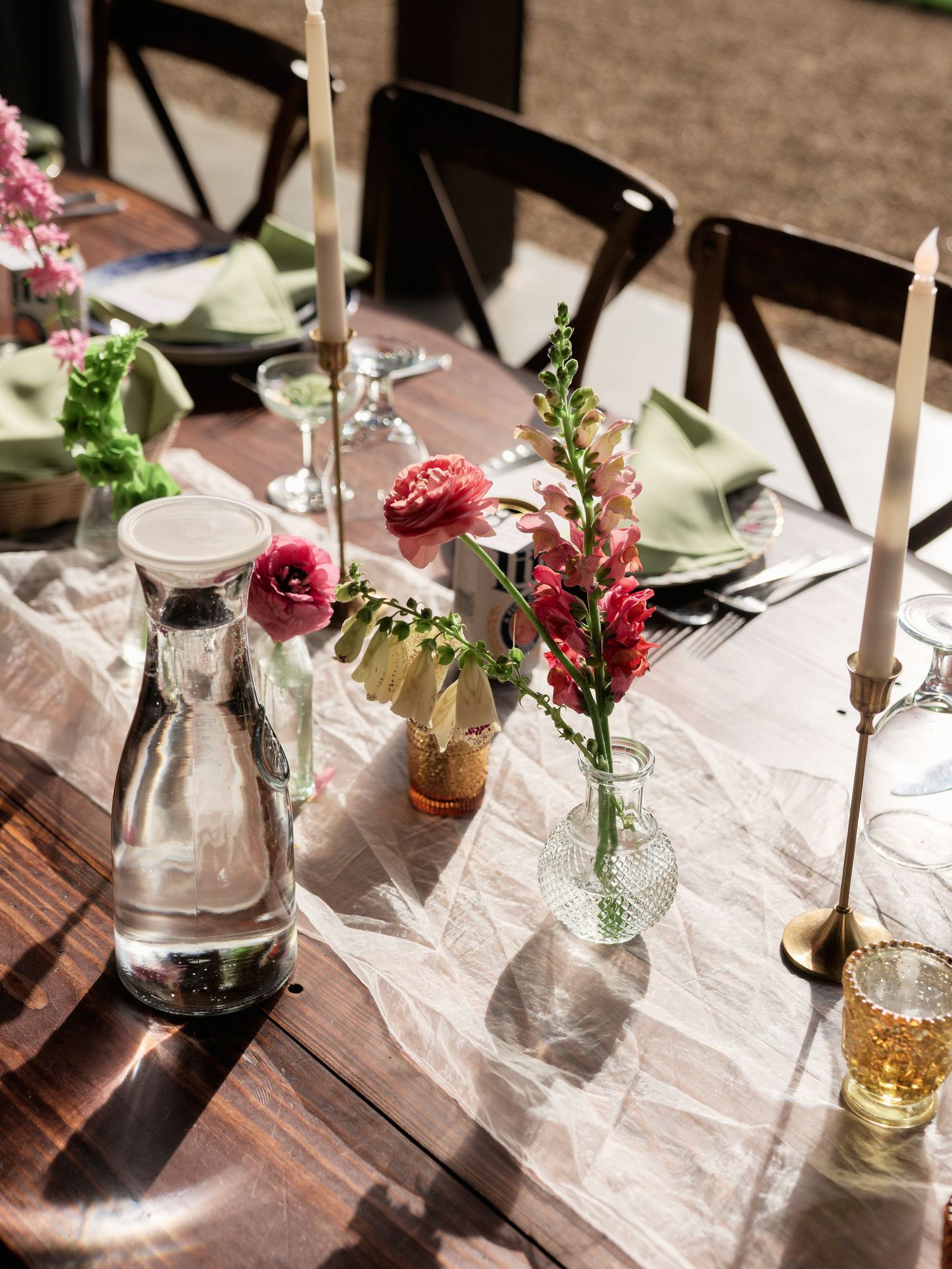 Intimate table setting with pink flowers, candles, and glass bottles on white linens.