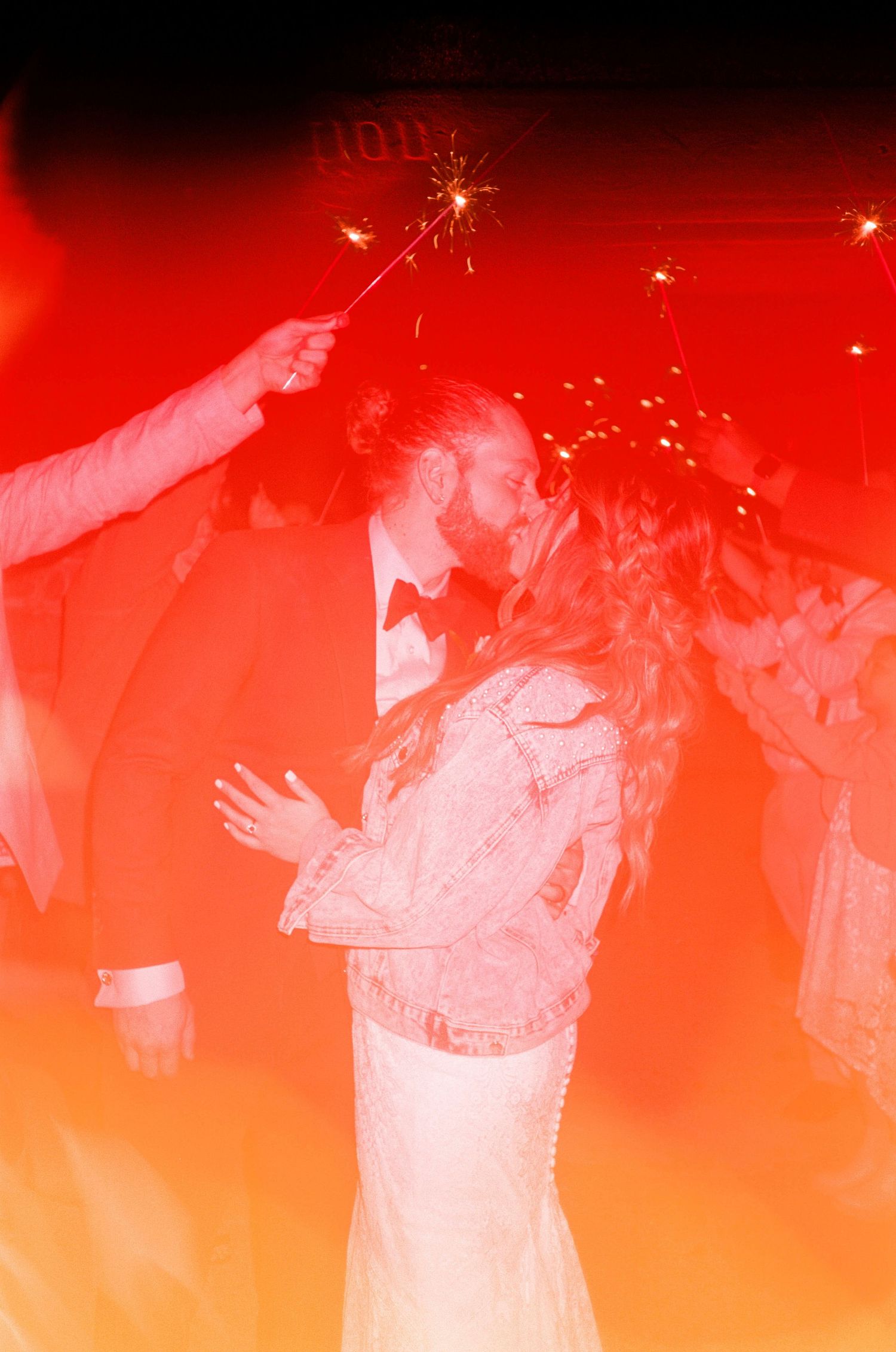 An artistic red-tinted wedding photo with sparklers creating a celebratory moment.