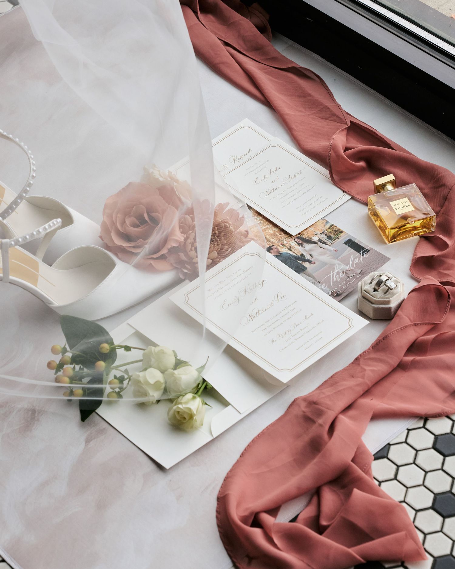 Elegant flat lay styling with dusty rose fabric, white stationery and delicate floral elements on marble surface.