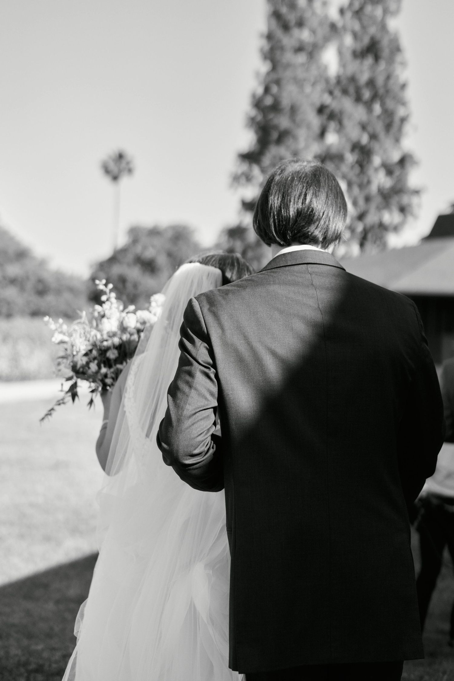 A black and white photo of a couple walking together with wedding bouquet.