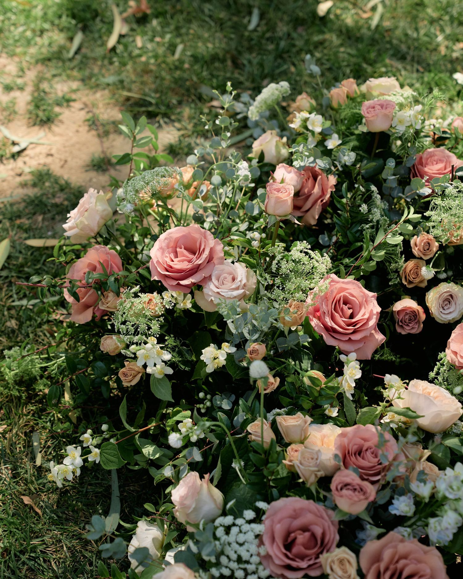 Lush garden-style floral arrangement with pink roses and mixed greenery in natural outdoor setting.