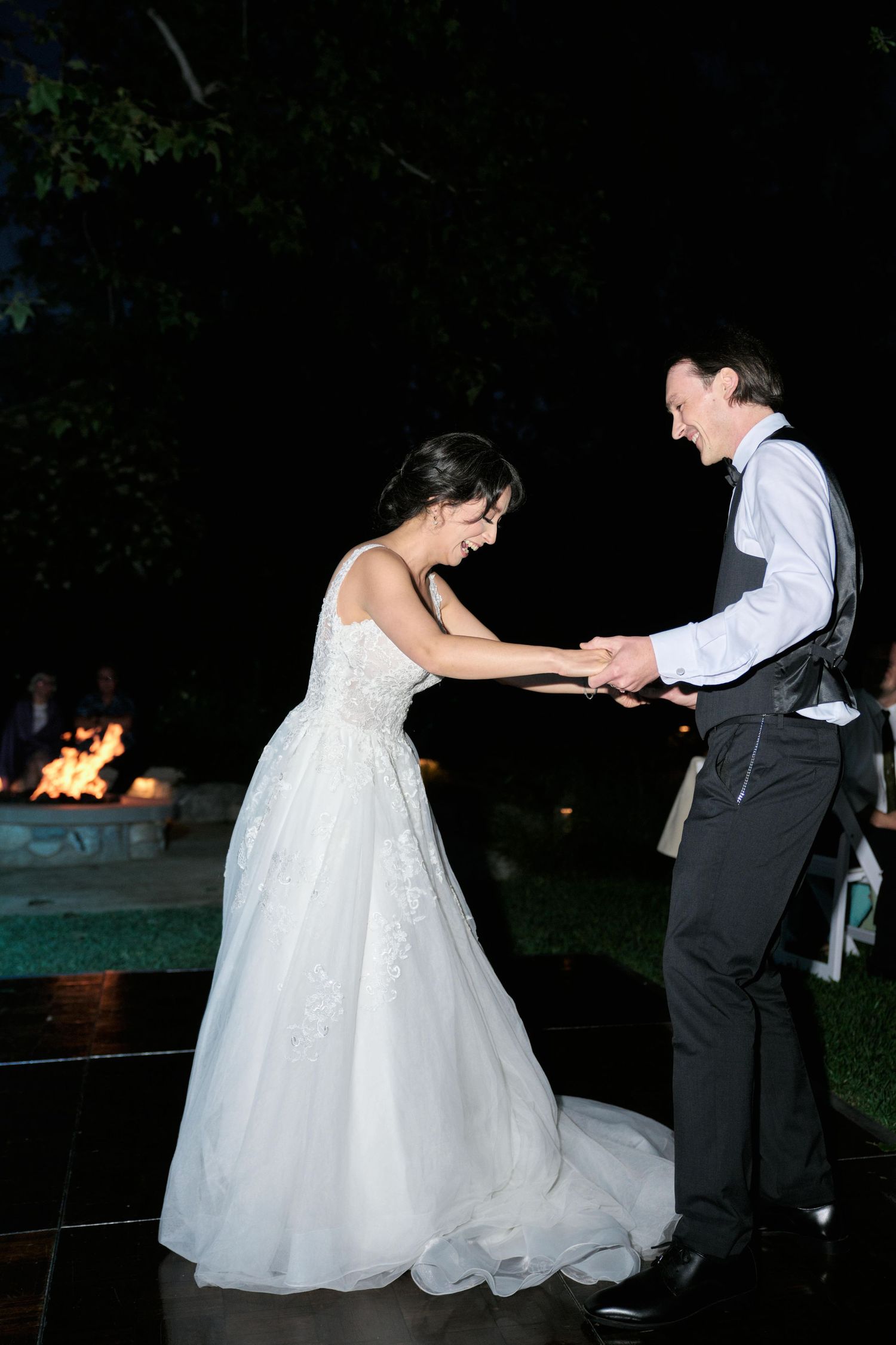 Romantic nighttime first dance at outdoor wedding with fire pit in background.