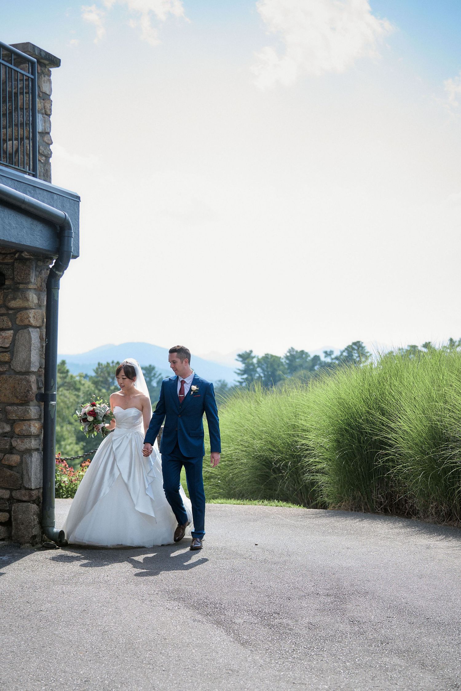 A wedding couple walking together on a stone path with mountain views in the background.