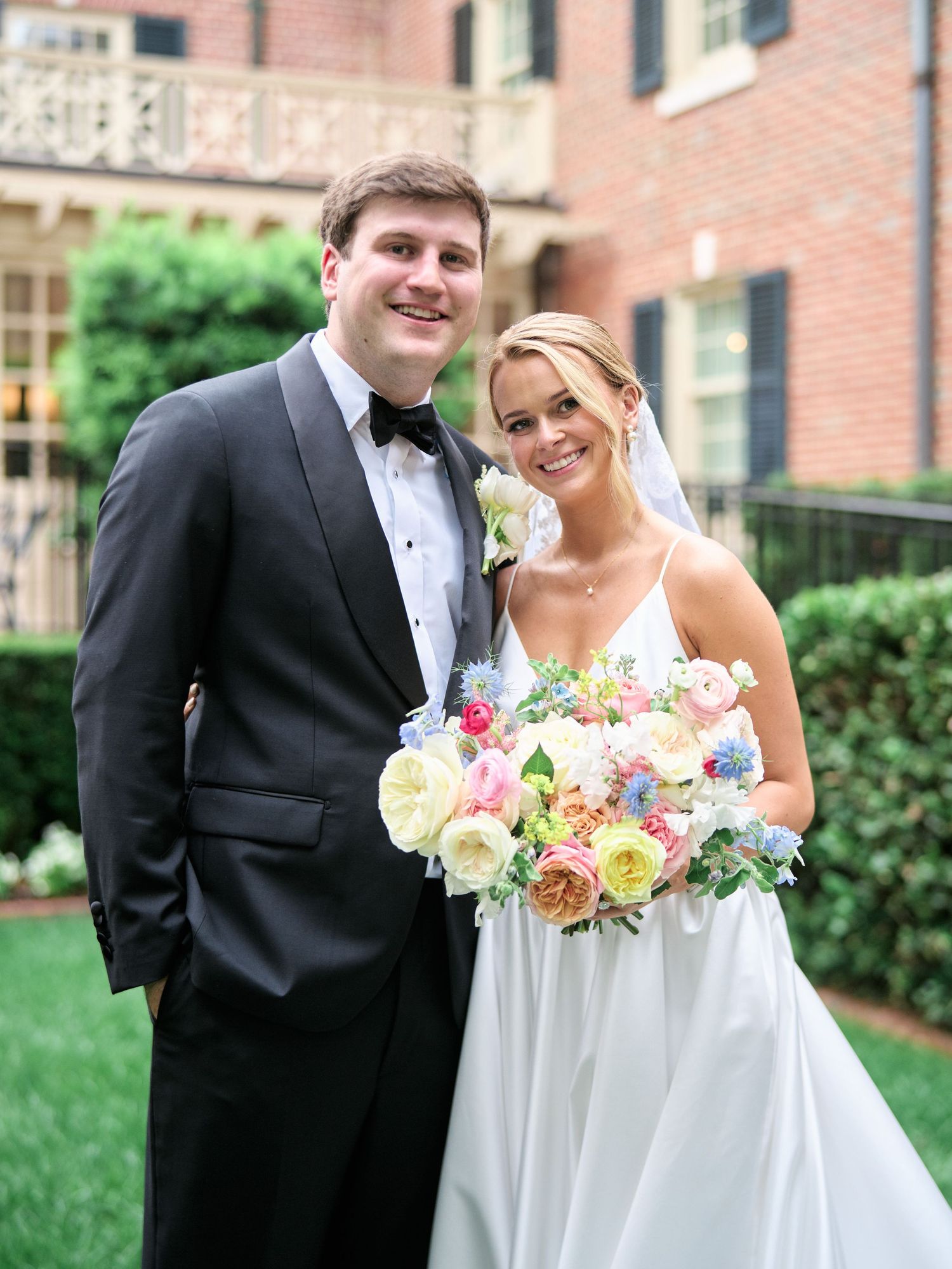 Wedding portrait featuring a colorful spring bouquet in front of a historic brick mansion.