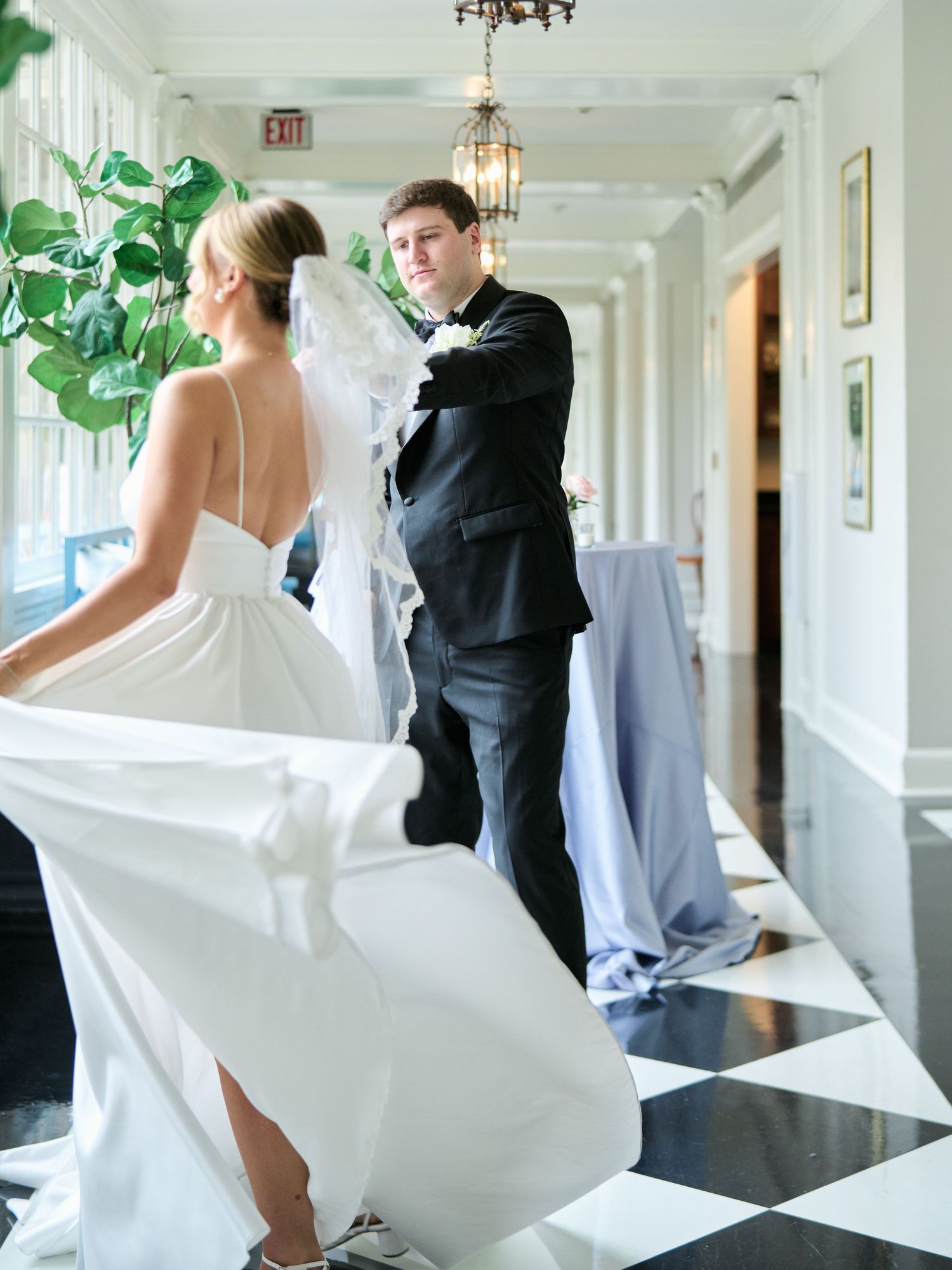 A couple twirls on a black and white checkered floor during their wedding dance, her white dress flowing elegantly.