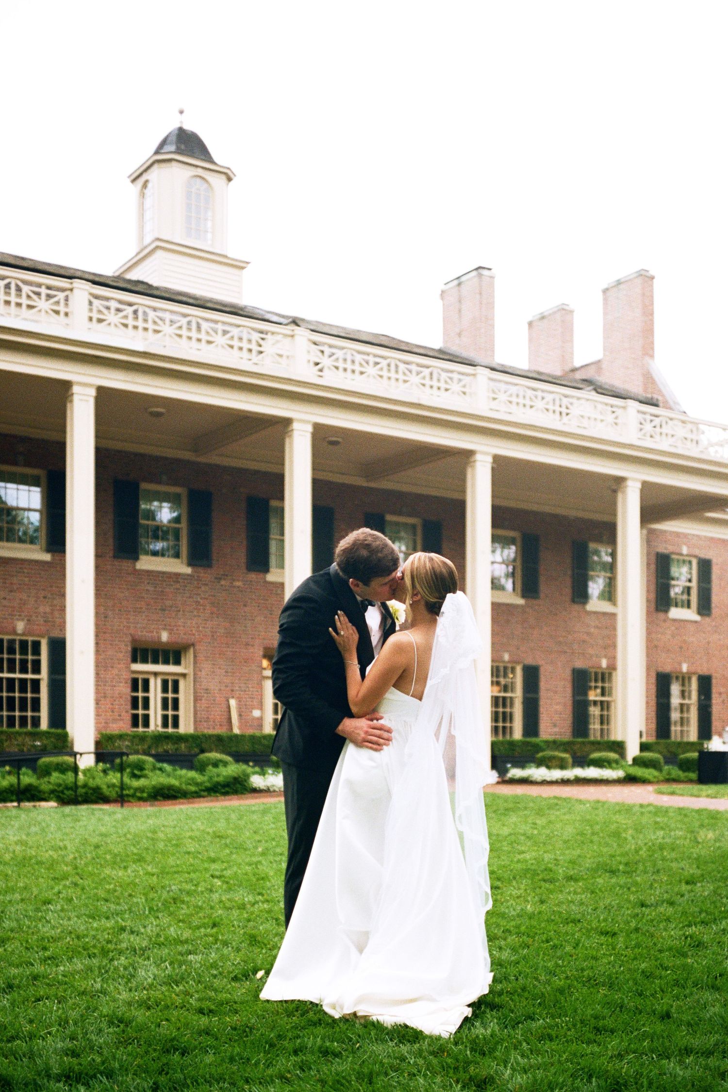 Elegant couple shares a romantic moment outside a grand colonial-style mansion with white columns.