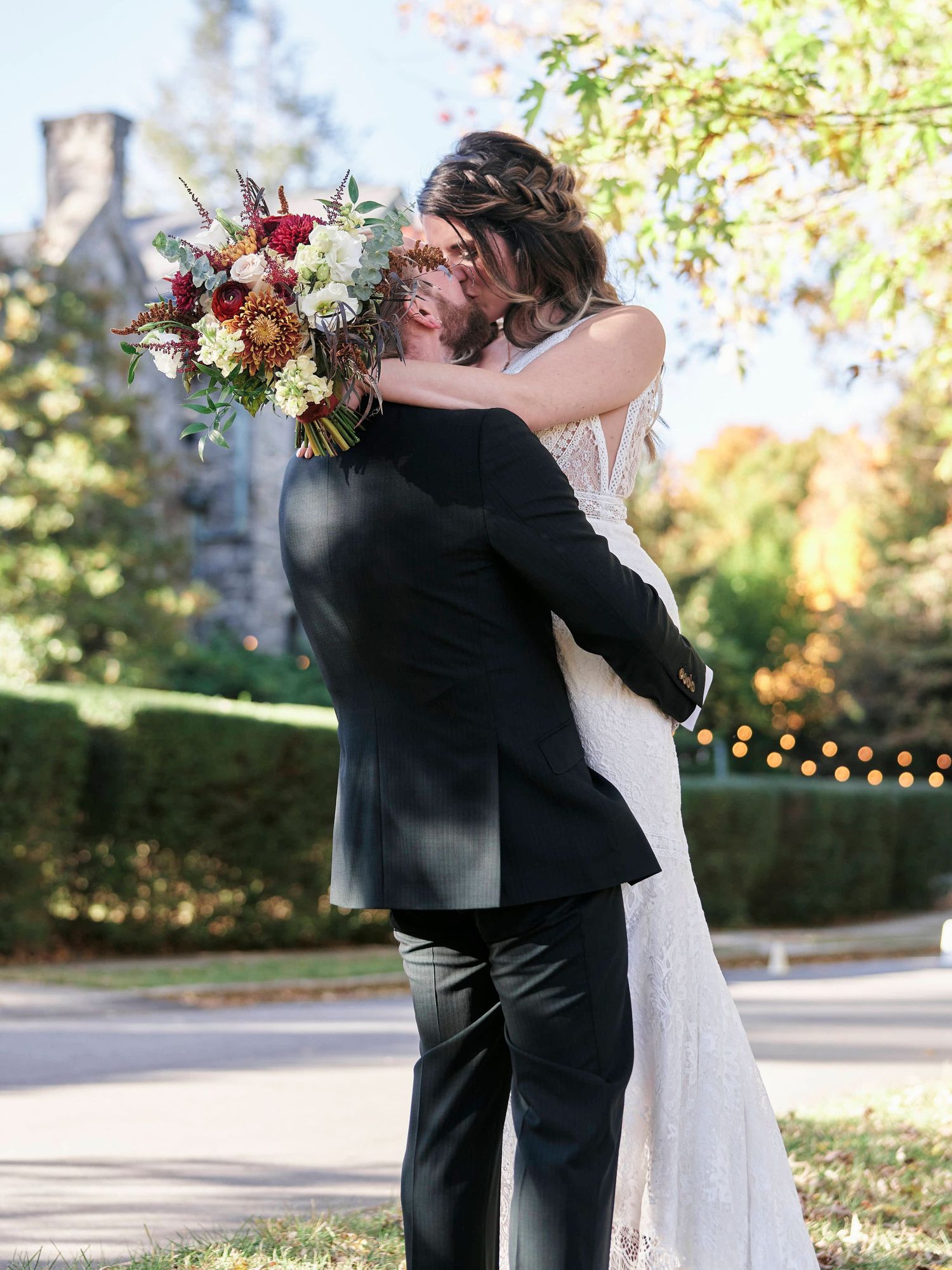 Newlyweds embrace while bride holds colorful autumn bouquet in garden setting.