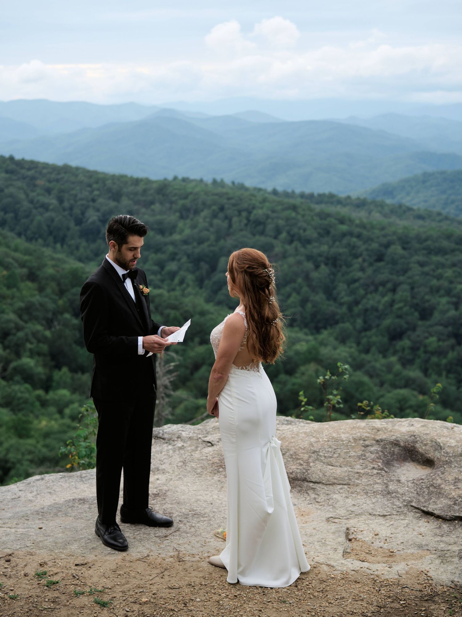 A couple exchanges vows during their intimate mountain-top elopement ceremony with panoramic views of rolling hills.